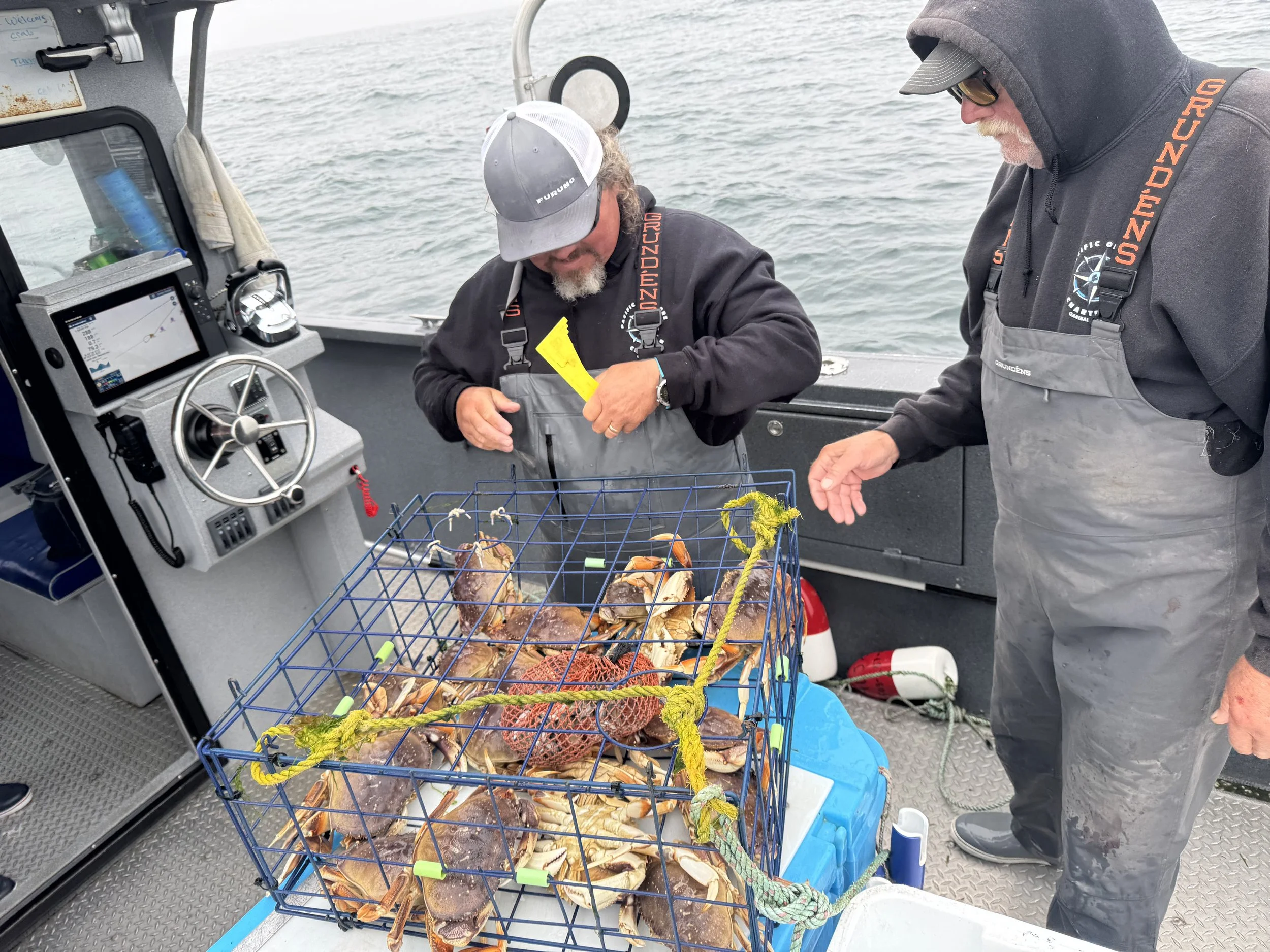 Two men inspecting a cage of crabs on a boat, with fishing equipment and water in the background.