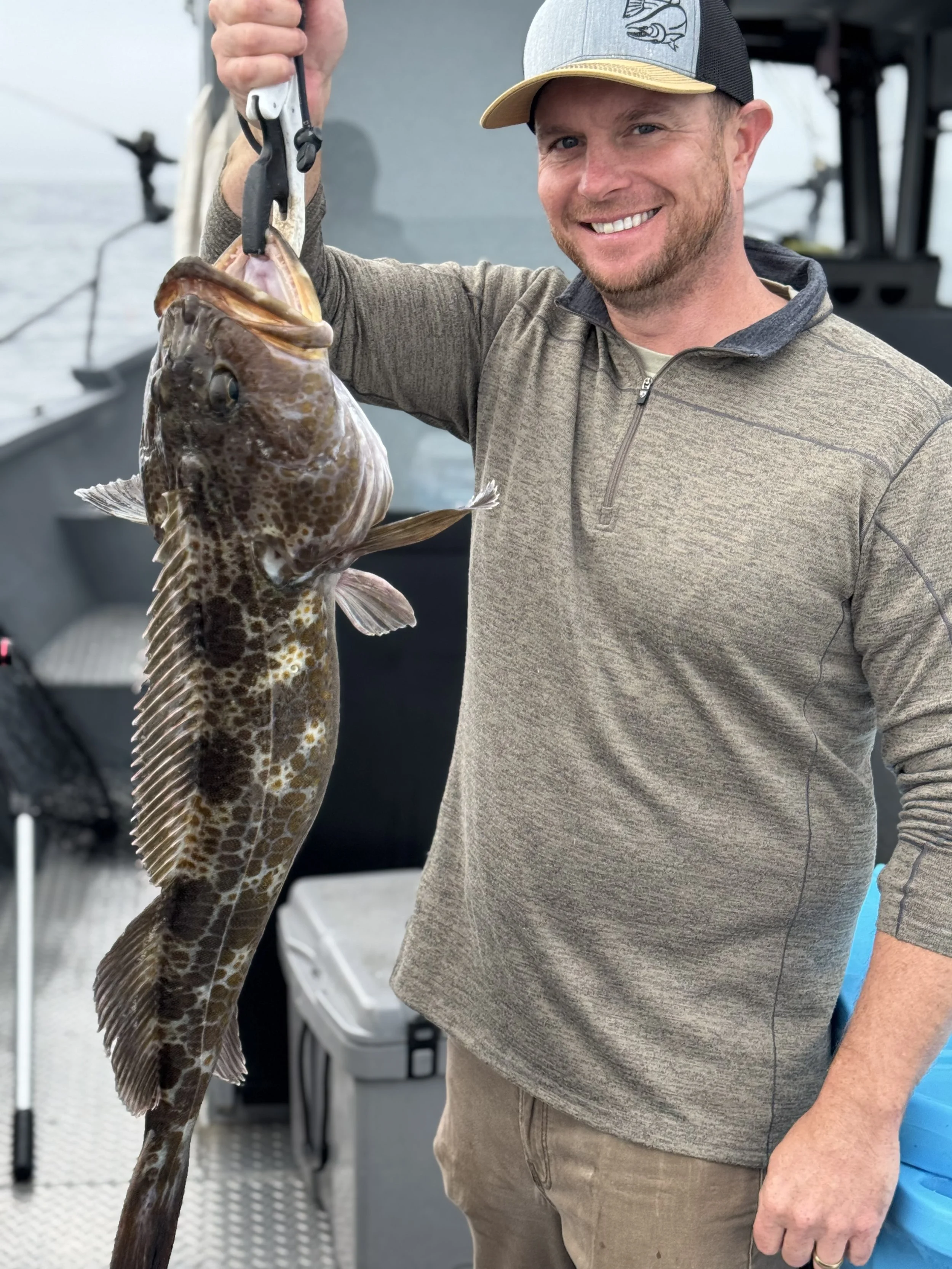 A man smiling and holding a large fish with a grip tool on a boat.
