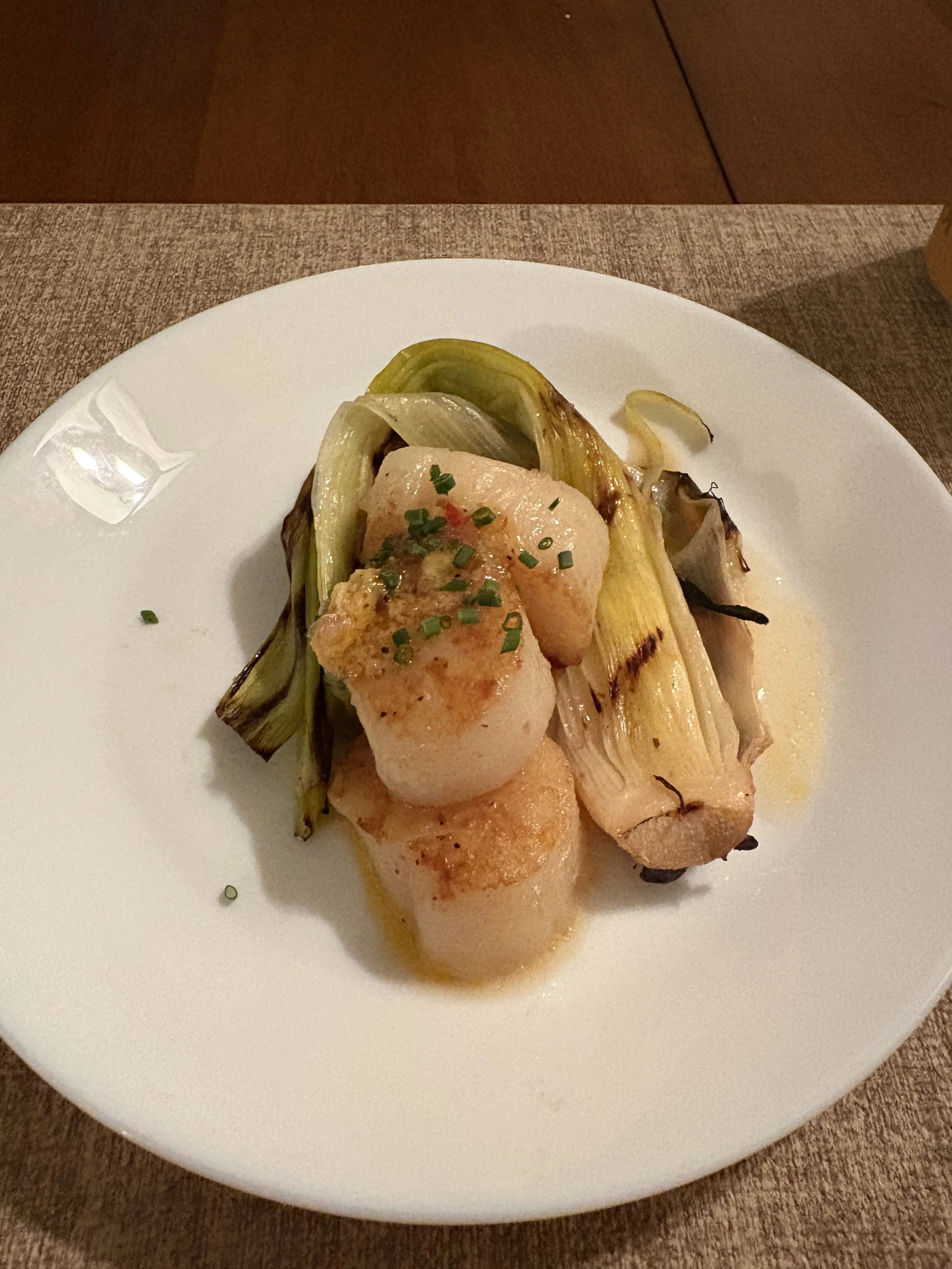 Seared scallops with grilled leeks on a white plate.