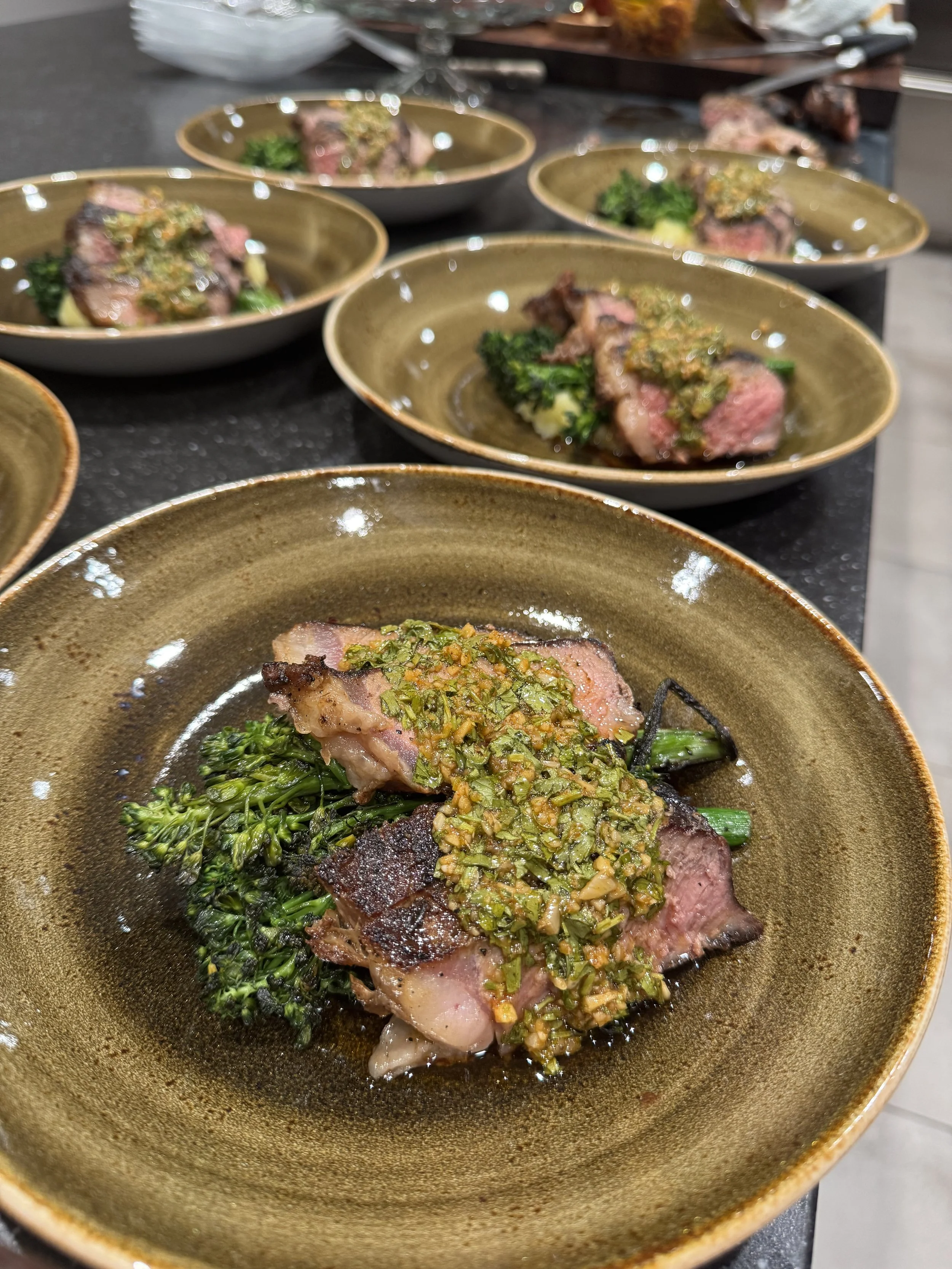 Close-up of a plate with a cooked piece of steak topped with herb sauce, served with green broccoli.