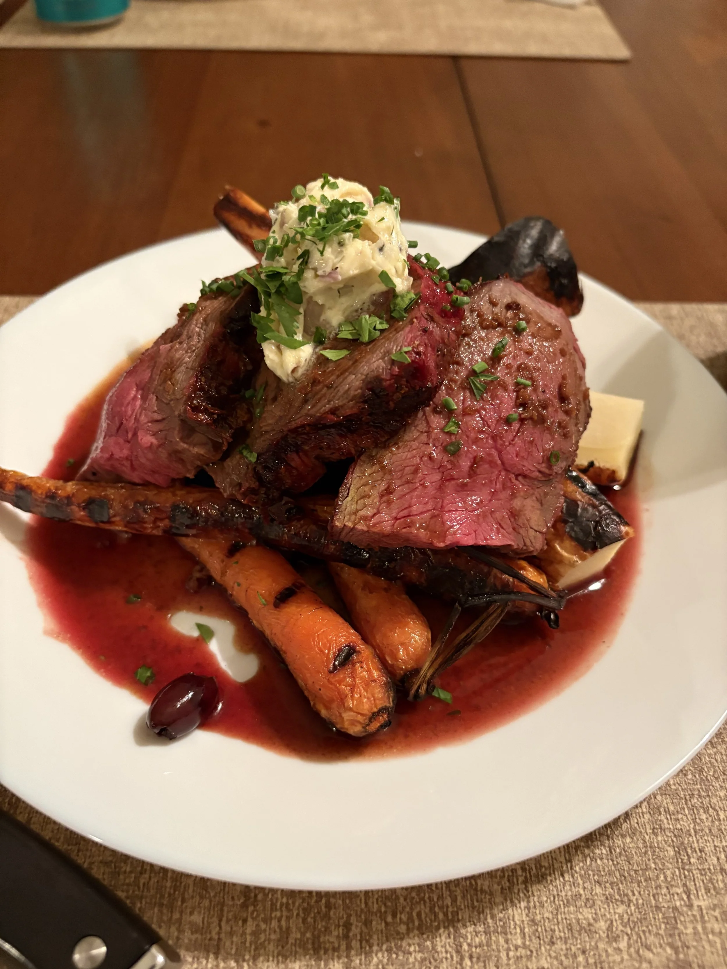Plate of prime rib with roasted carrots, potatoes, and a dollop of herb butter, garnished with chopped herbs.