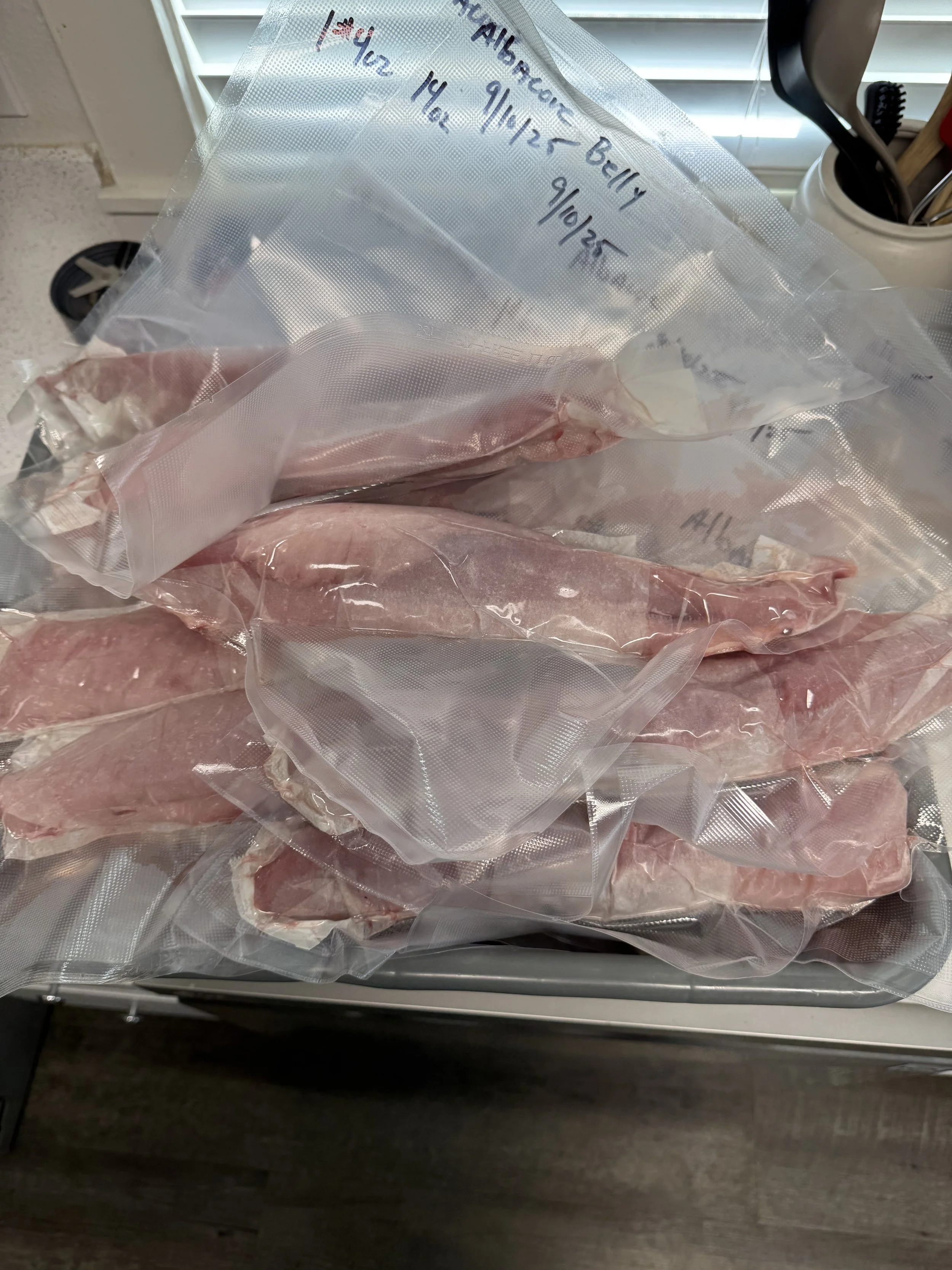 A ziplock bag containing raw meat, with handwritten labels indicating dates and names, placed on a countertop near a utensil holder with cooking tools.