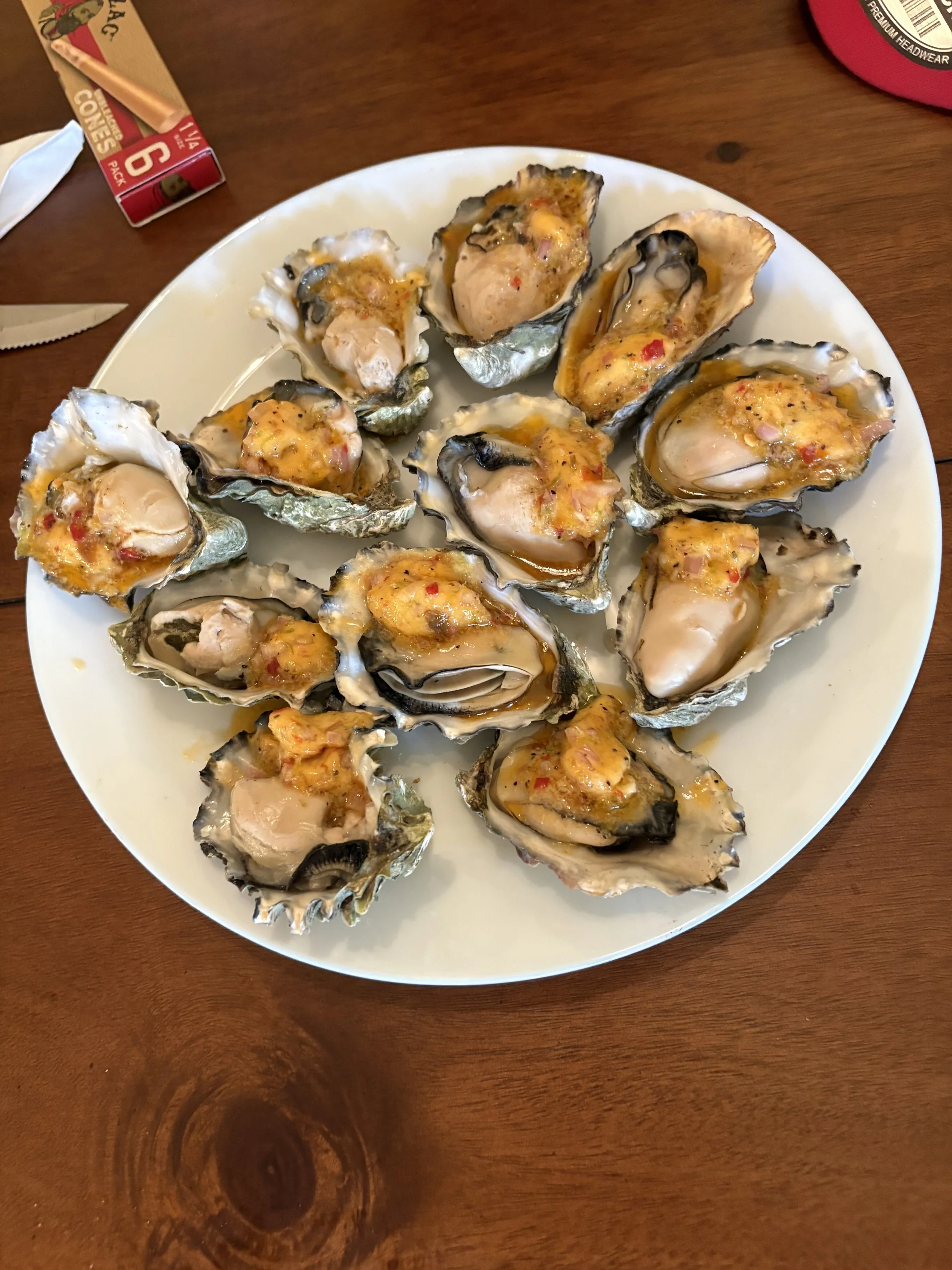 A plate of baked oysters topped with cheese and red pepper flakes on a wooden table.