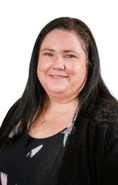 Portrait of a woman with long dark hair, smiling, wearing a black top and blazer, against a white background.