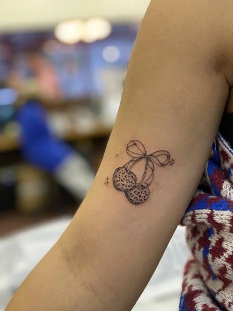 Tattoo of two cherries with leopard print on the skin of an arm.