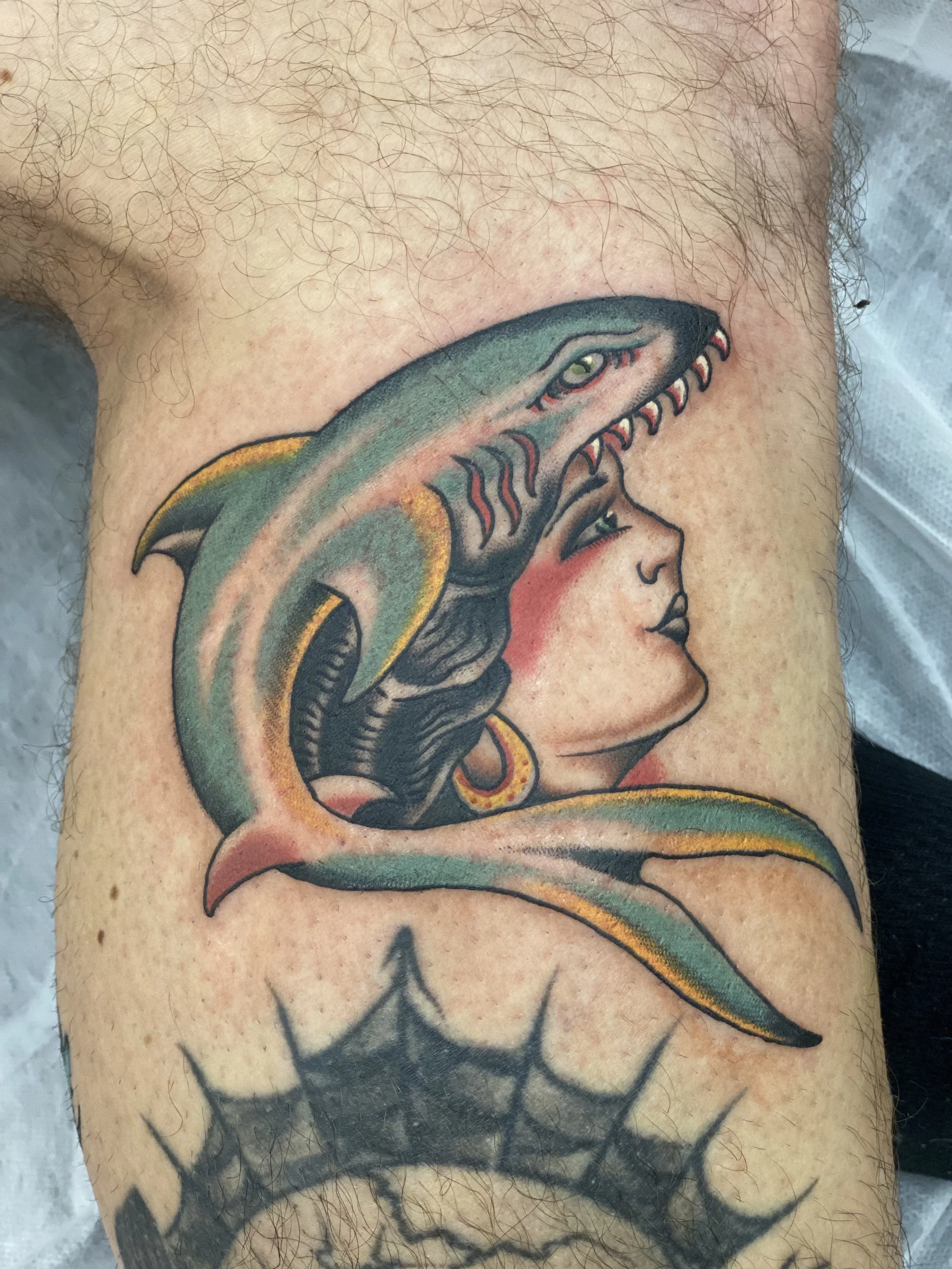 A tattoo of a girl with angel wings on her back, with a snake wrapped around her head. The girl is depicted with profile view, with short hair and a serene expression.