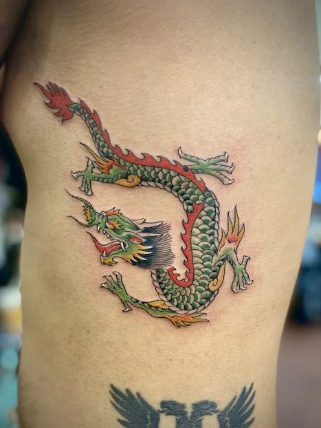 Colorful dragon tattoo on person's side with detailed scales and fierce expression.