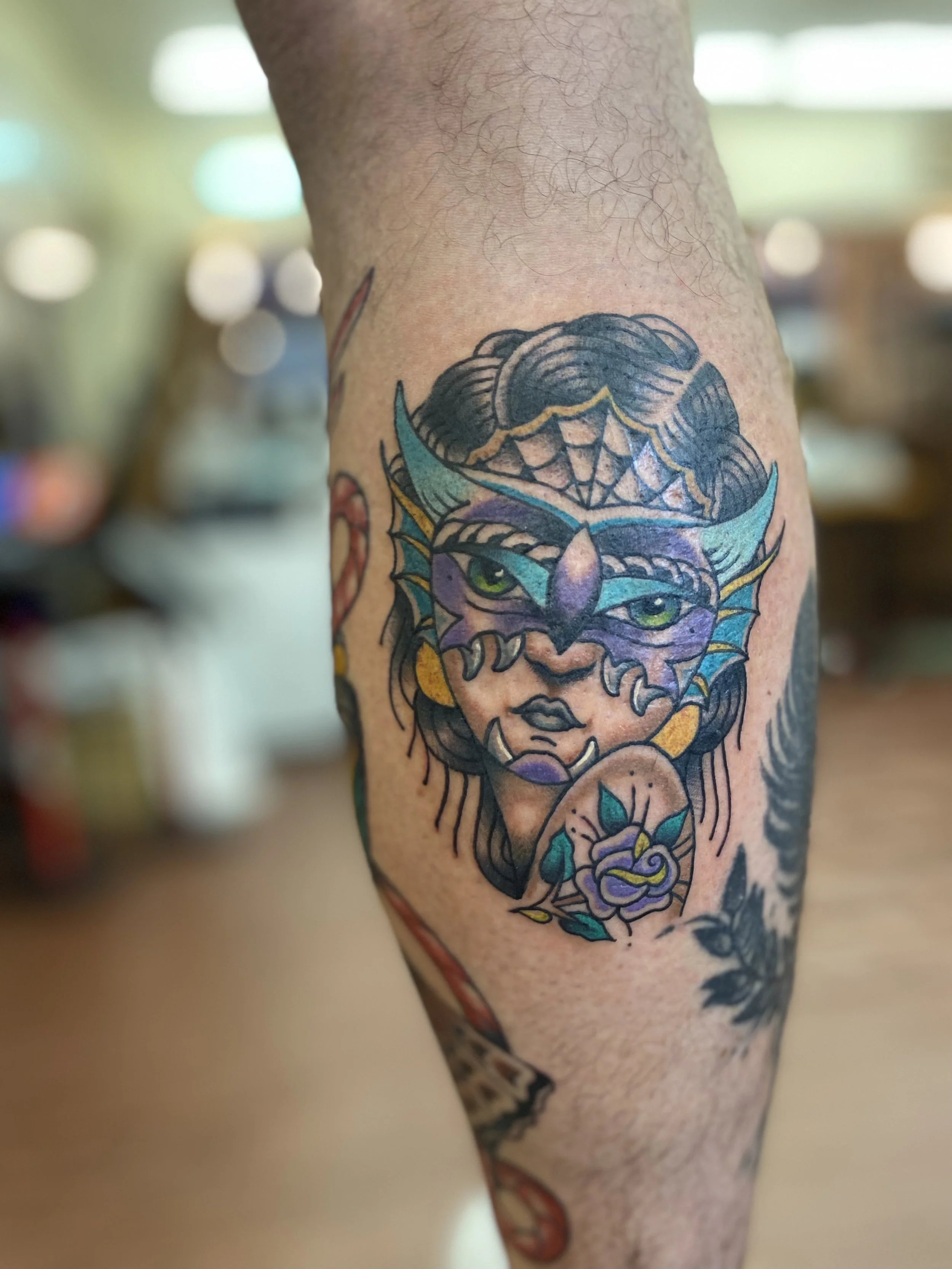 Colorful tattoo of a woman's face with large eyes, dark hair, and floral elements on the person's arm.