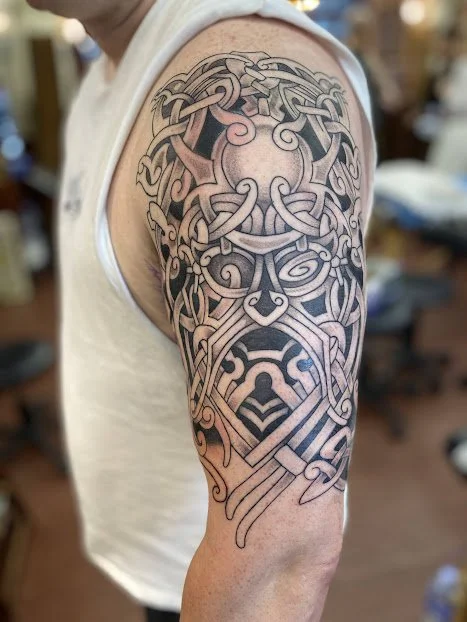 A Nordic style god mask tattoo featuring an image of Odin and Jormungandr on a man's bicep. cool