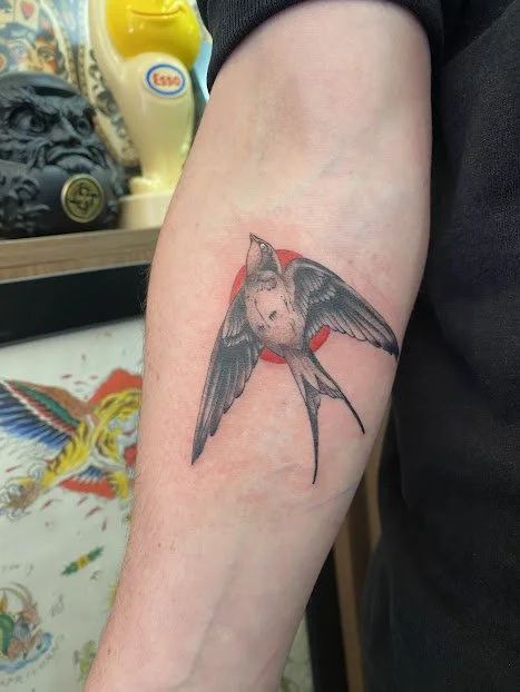 Tattoo of a bird with outstretched wings on a person's arm, with a red background behind it.
