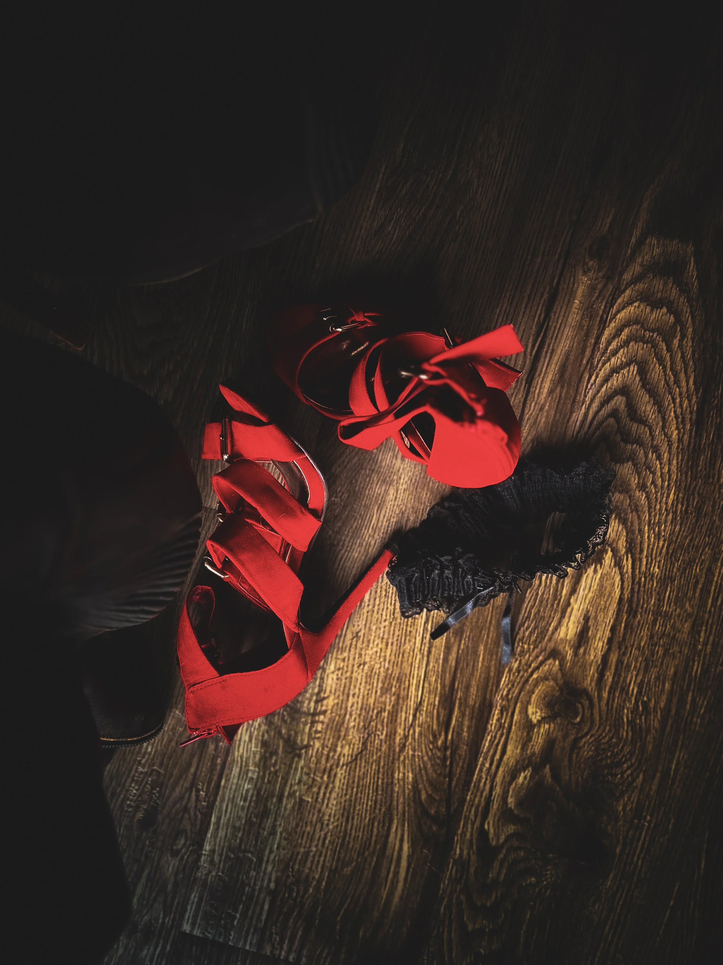 Red high-heeled shoes with ankle straps on a wooden floor