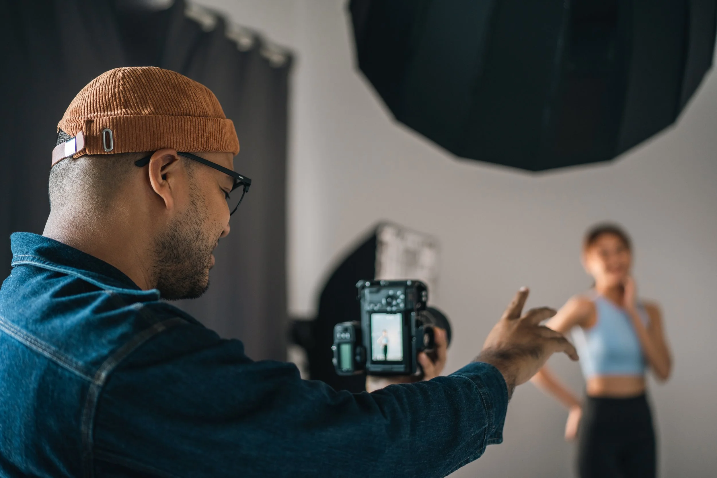 Photographer taking a photo of a woman posing, with studio lighting and backdrop in the background.