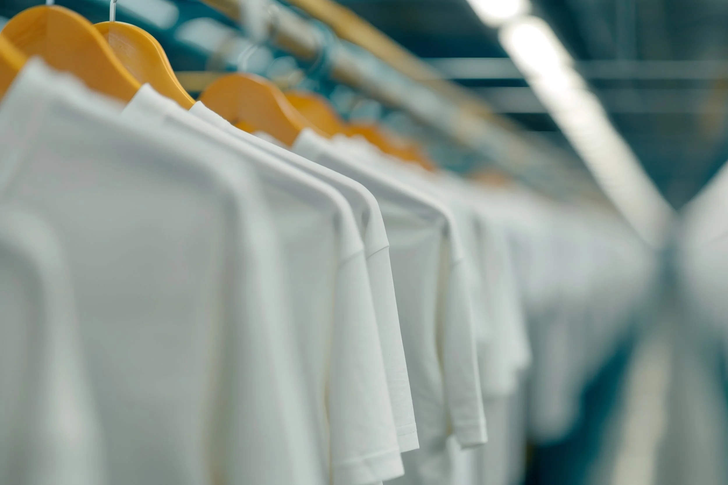 White T-shirts hanging on yellow hangers on a clothing rack.