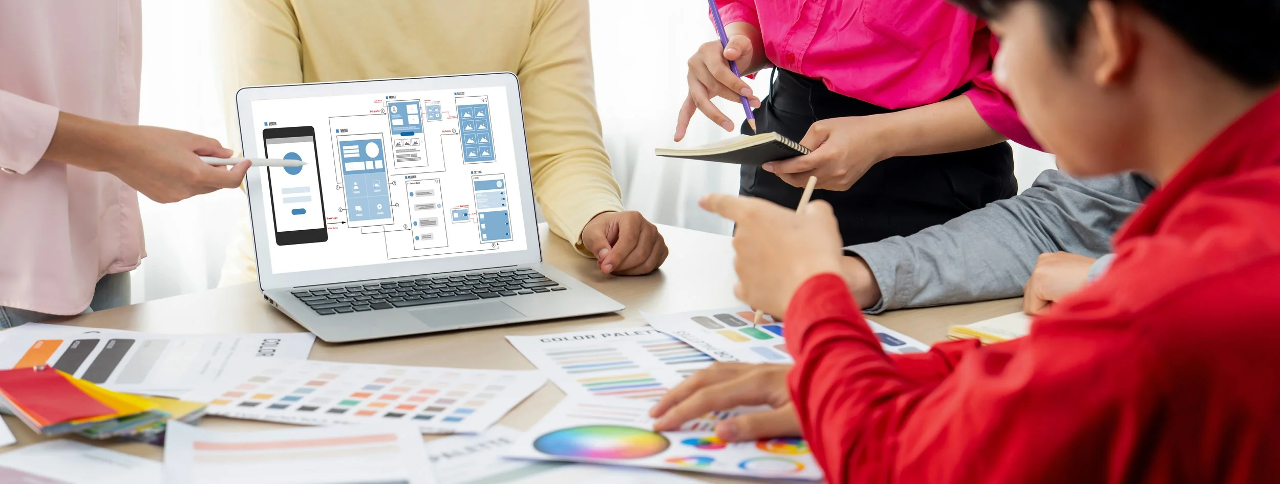 People engaged in a collaborative graphic designing session with a laptop, color palettes, and design sketches on the table.