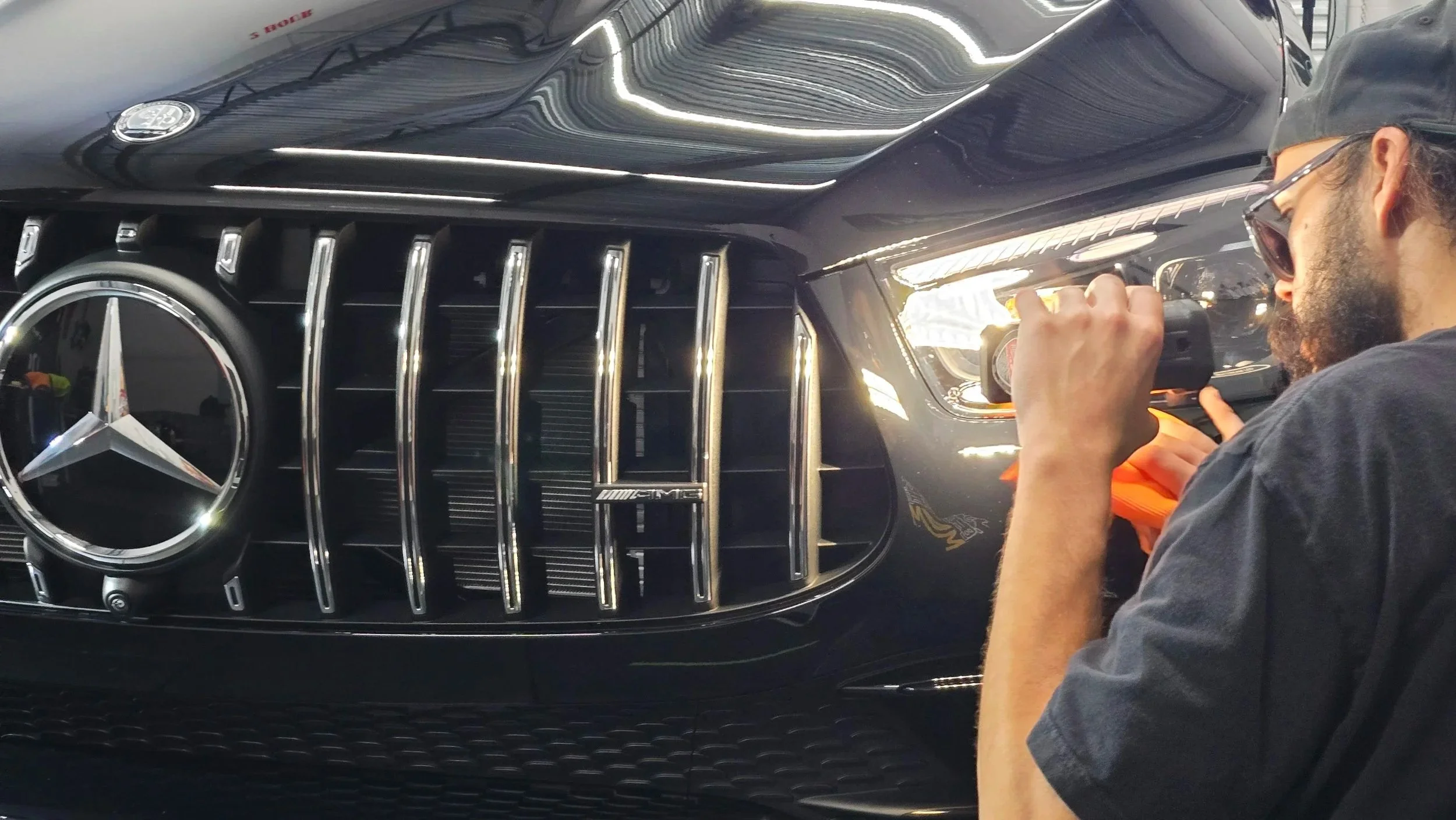 Professional detailer inspecting the flawless paint finish on a black Mercedes-AMG GLE 63 S after a 25-year self-healing ceramic coating installation.