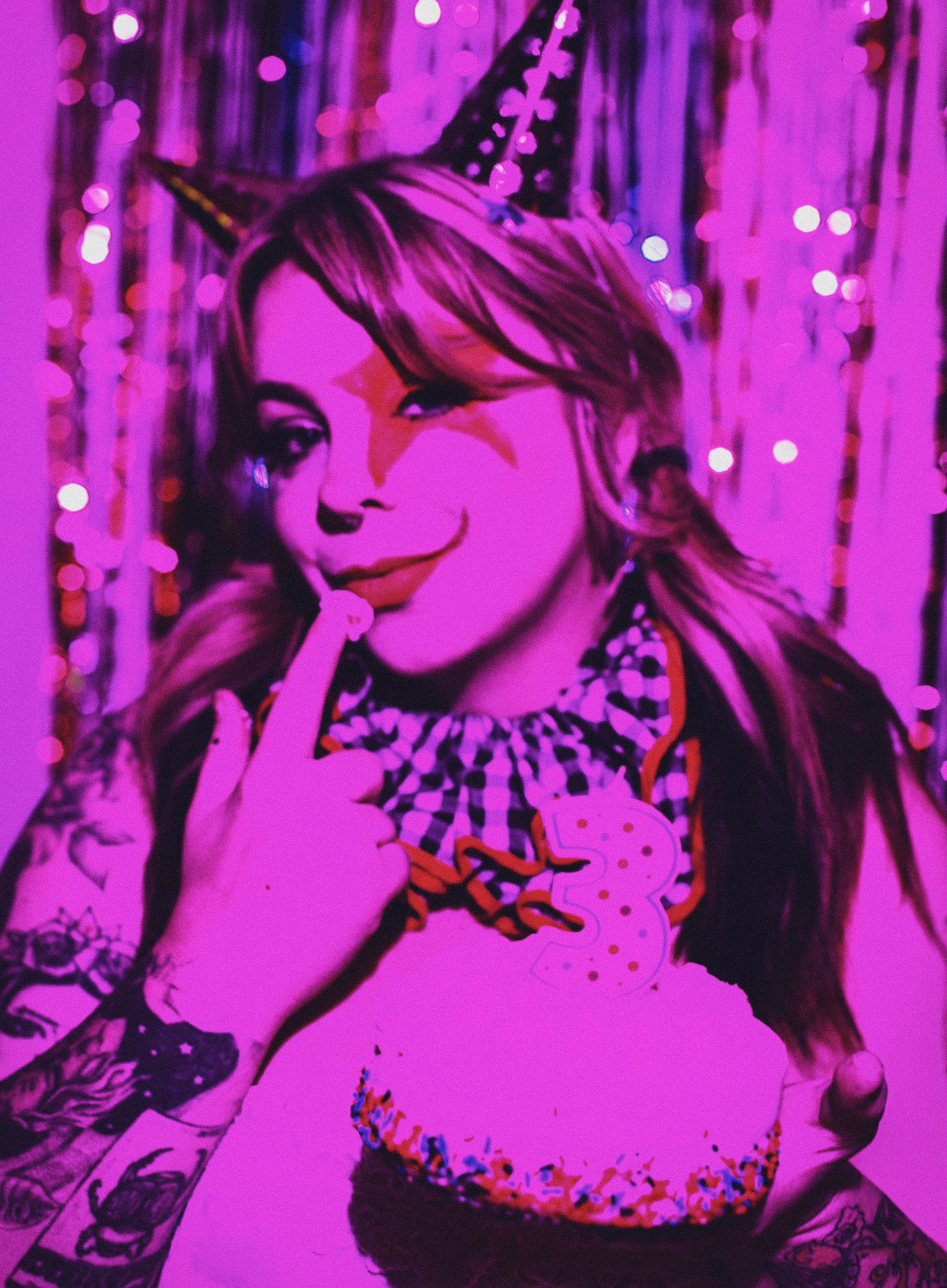 Portrait of a woman celebrating her 33rd birthday, wearing a witch's hat with a pollera and a necklace with the number 33, surrounded by purple and pink decorations and fairy lights.