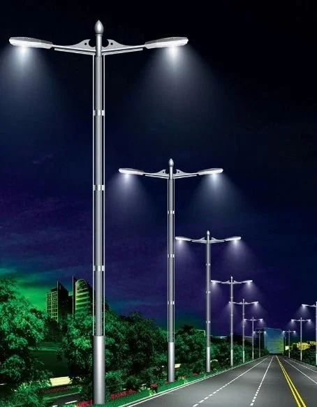 A row of modern streetlights illuminating a road at night with city buildings and trees in the background.