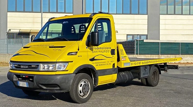 Camion giallo per demolizioni con scritte pubblicitarie, parcheggiato in strada in un'area urbana.