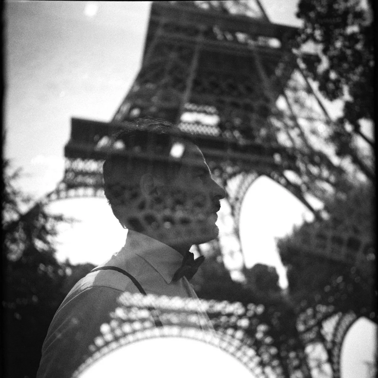 Silhouette of a man in a tuxedo and glasses reflected on a glass surface, with the Eiffel Tower in the background.