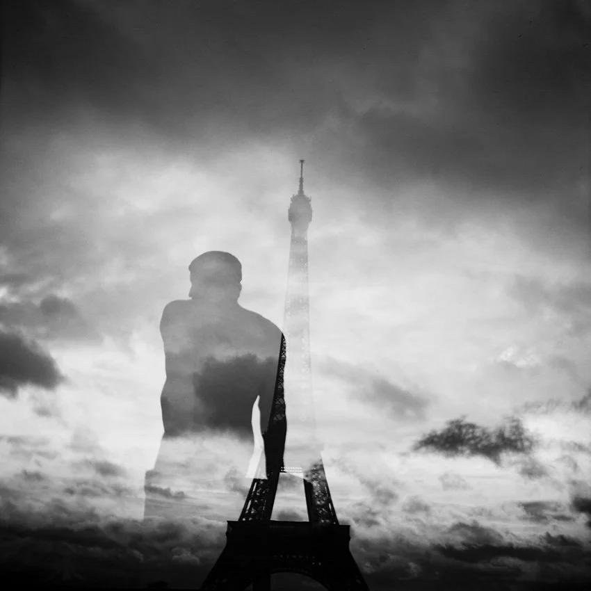 Black and white double exposure photo of a person and the Eiffel Tower against a cloudy sky.
