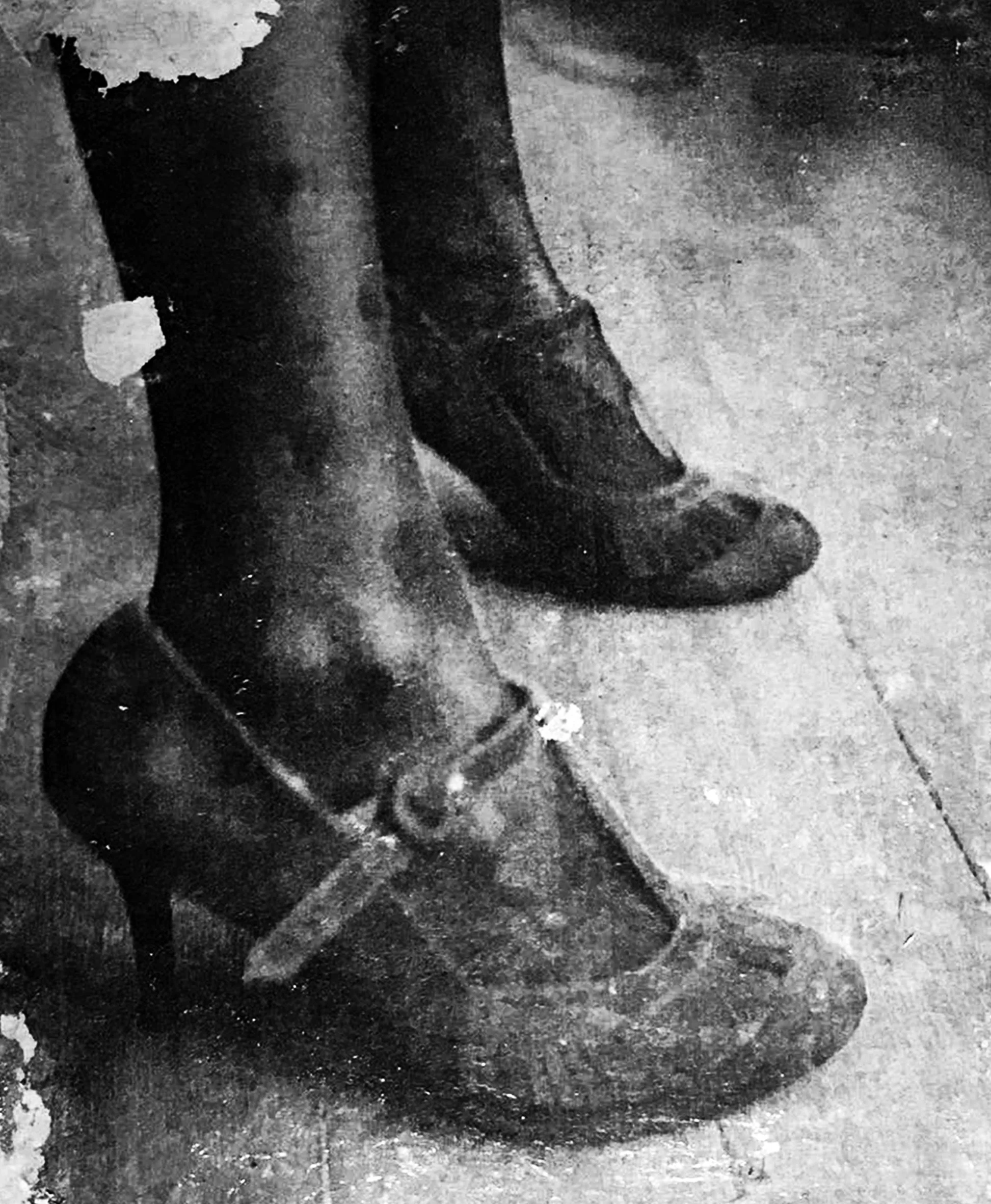 Black and white photo of person wearing heeled ankle boots standing on a sidewalk.