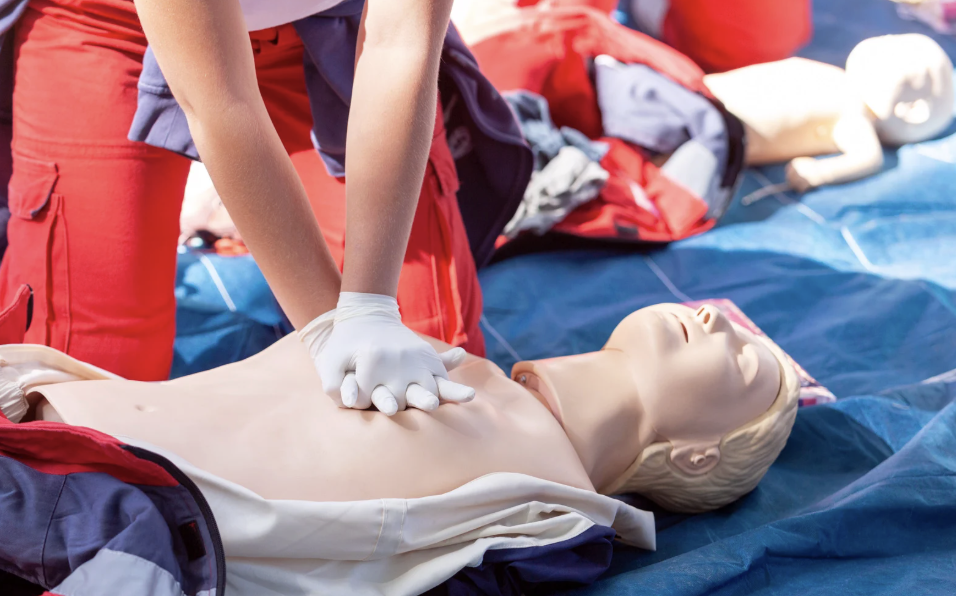 Closeup of a person wearing orange pants and performing CPR on a dummy