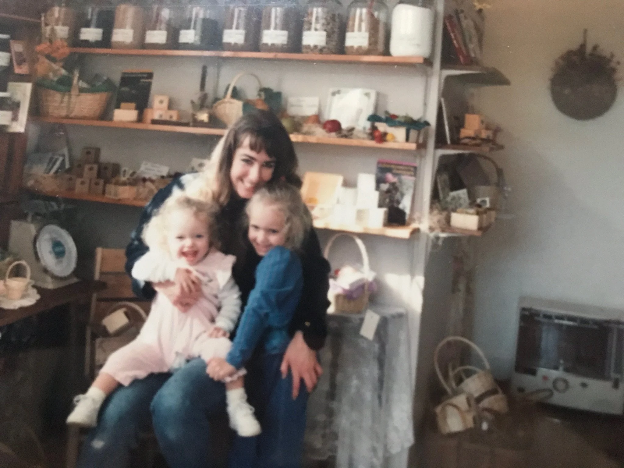 Take in the early 1990s, Forever Green owner Melanie Restall is seated in front of a wall of shelves in her shop with her two daughters held close