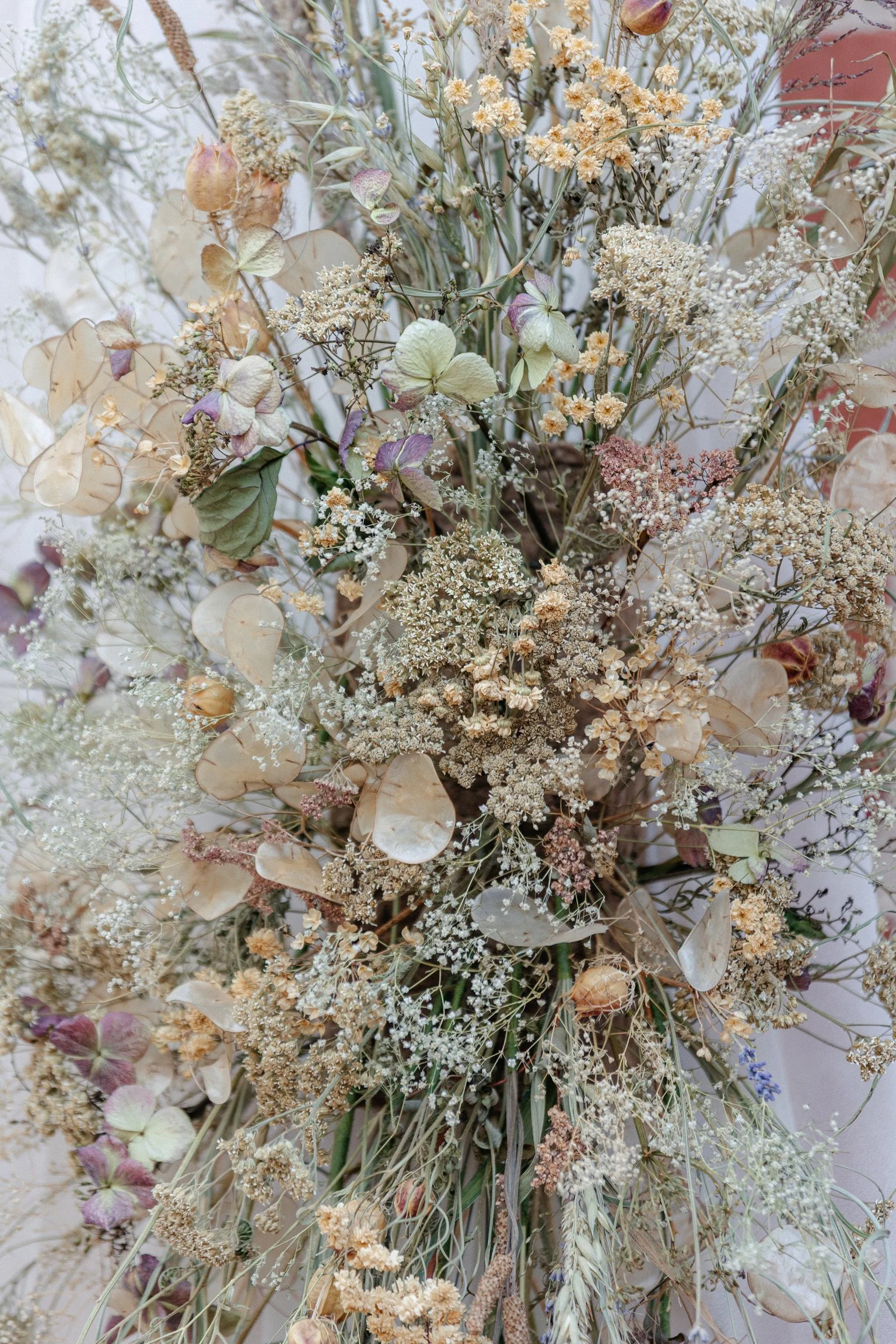 A floral arrangement of dried flowers and leaves in neutral and muted tones, including beige, cream, and purple hues.