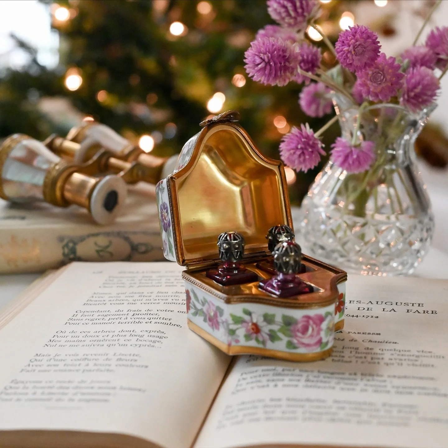 This is a beautifully hand-painted Limoges trinket box adorned with delicate floral motifs and finished with a sculpted bow clasp. Inside, three petite glass perfume bottles nestle perfectly within the box, each topped with a jeweled stopper that cat