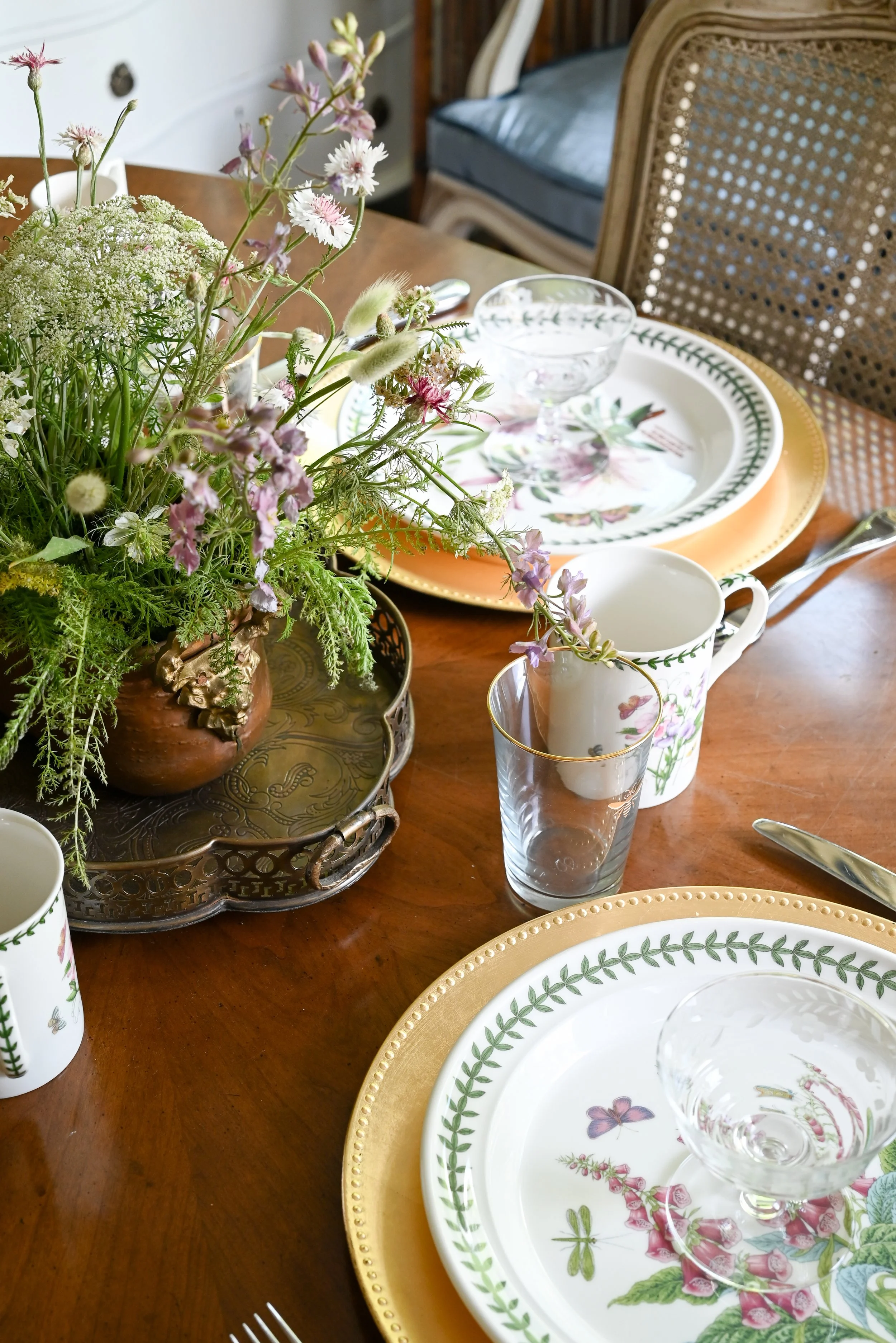 Collected table setting with Portmeirion botanical plates, gold charger, crystal glassware, and wild garden clippings in an antique brass tray