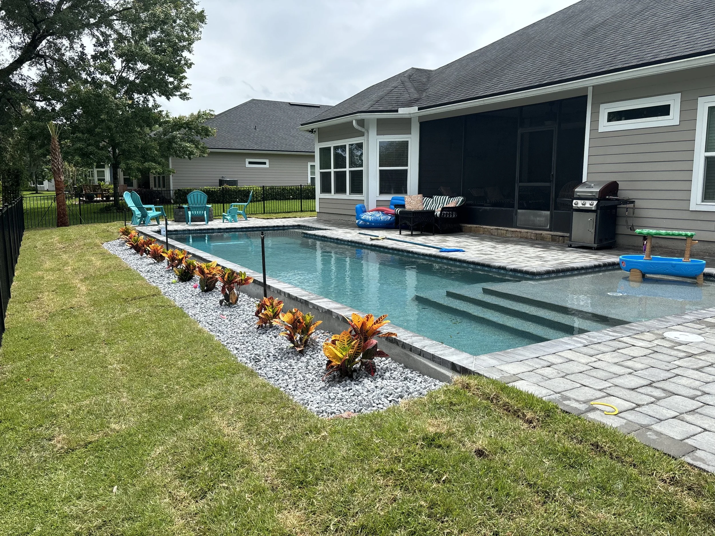 Modern Backyard Pool with Sun Shelf & Outdoor Lounge  Blue Water Outdoors  Butler Beach, FL
This custom in-ground pool by Blue Water Outdoors blends sleek design with everyday comfort, featuring a shallow lounging area with submerged seating and a de