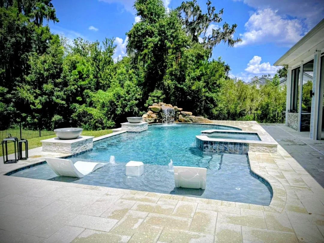 Experience the pinnacle of outdoor living with this custom-built luxury swimming pool by Blue Water Outdoors. Featuring a multi-tiered design, the pool includes a shallow sun shelf with submerged lounge chairs, a deep swimming area, and an elevated s