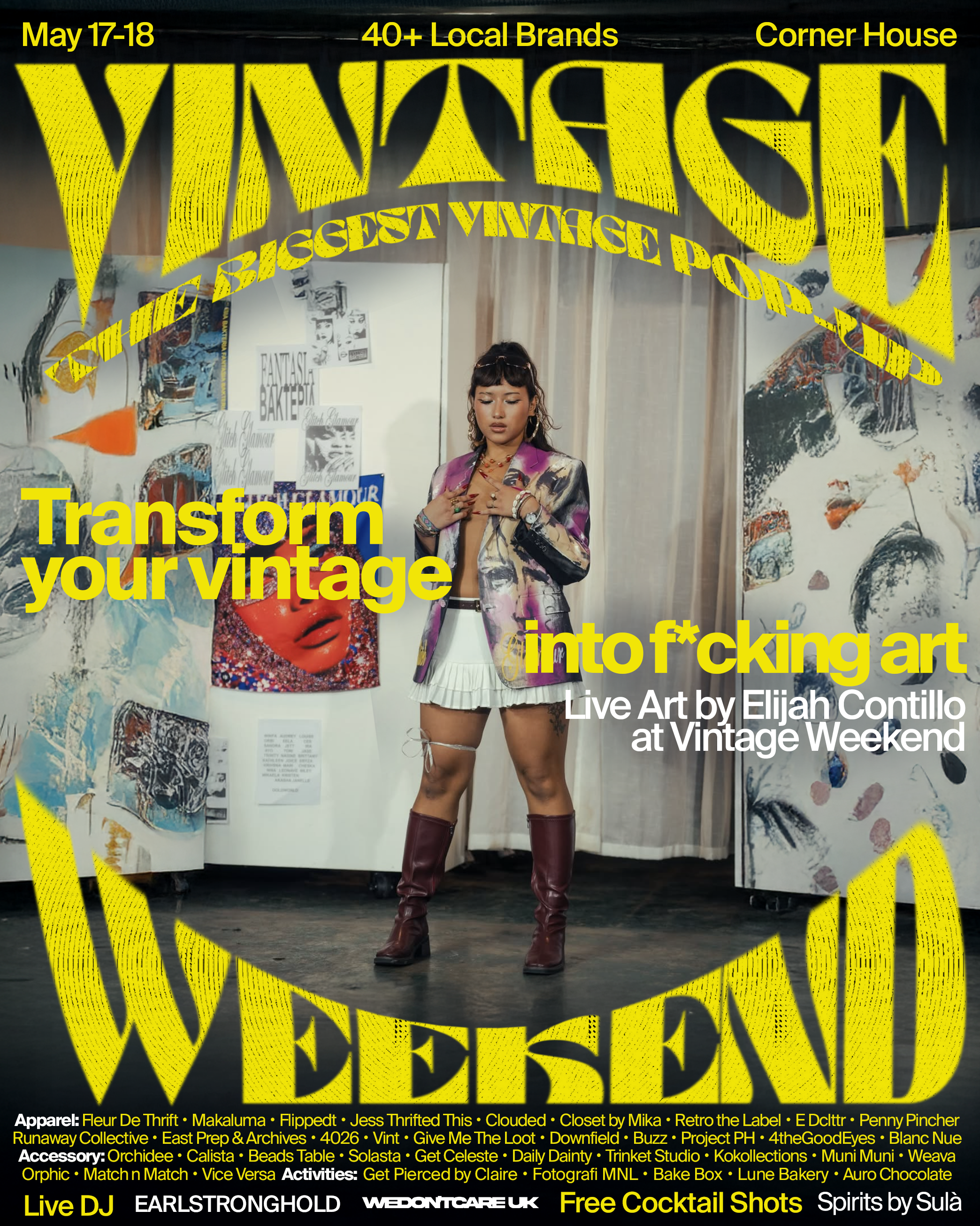 A woman stands in front of an art display at Vintage Weekend, surrounded by colorful artwork, wearing a patterned blazer, white skirt, and maroon boots.