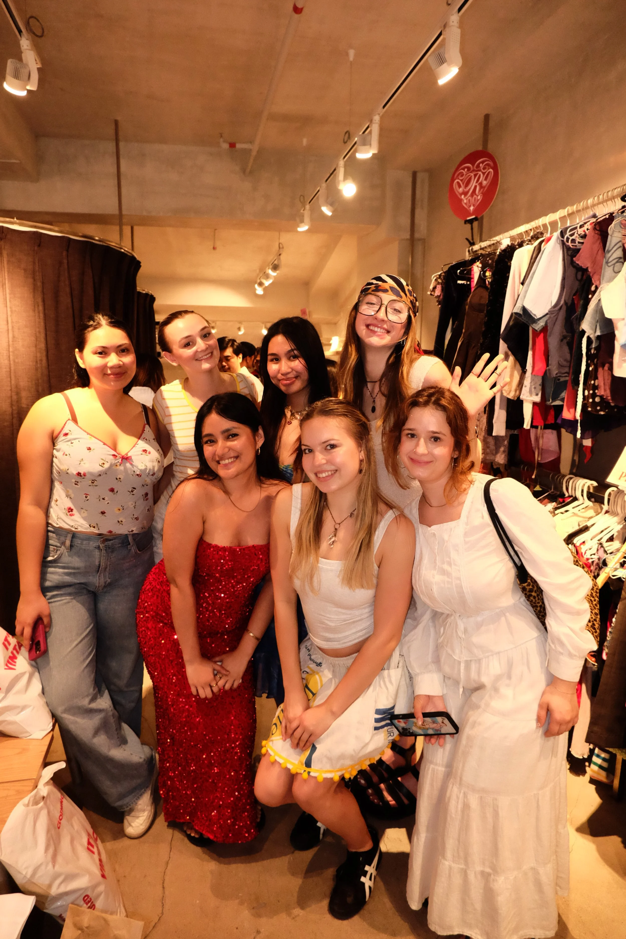 Group of women smiling and posing for a photo in a clothing store fitting room area.