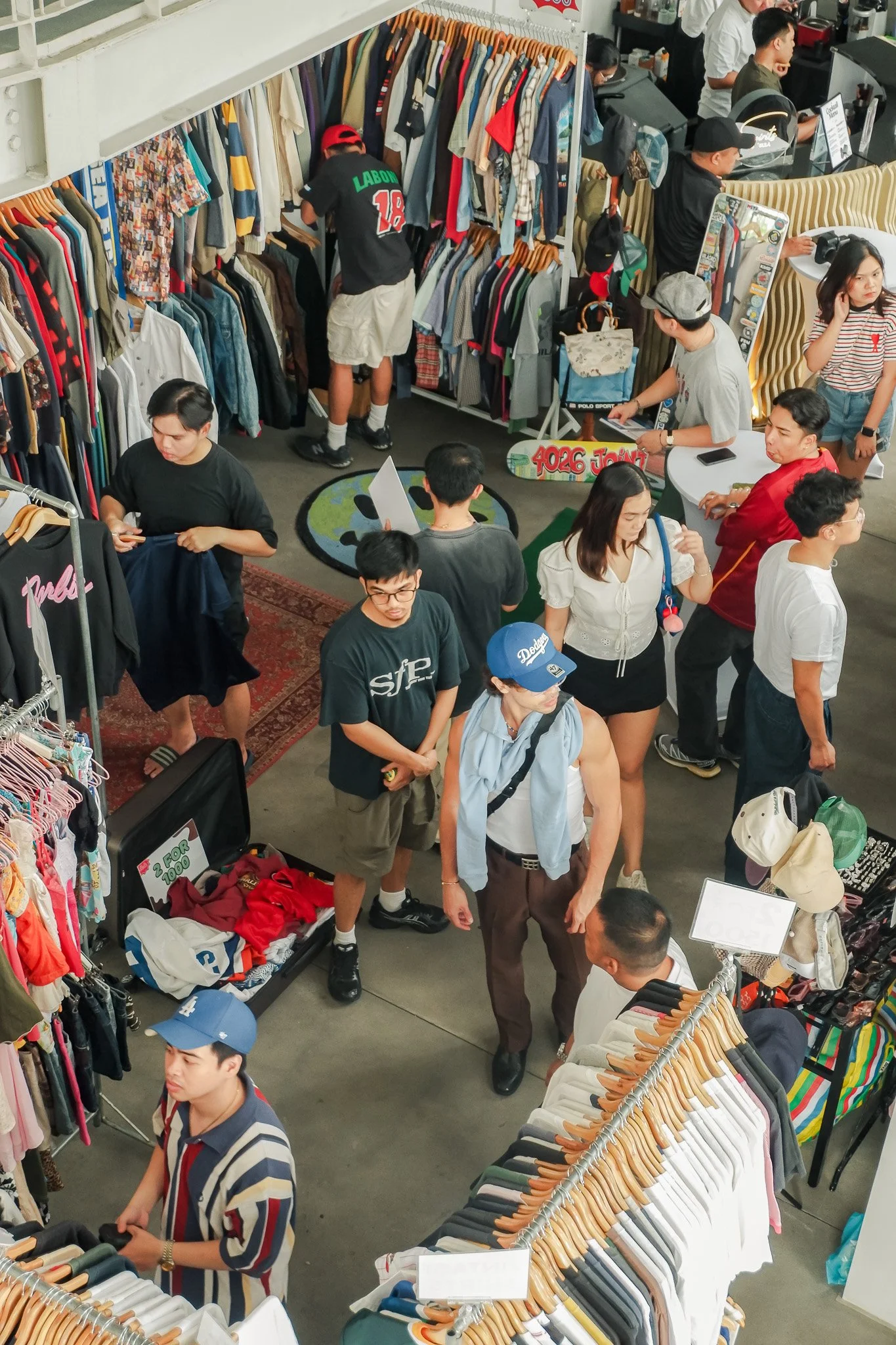 Crowded thrift store with clothing racks, customers shopping, and a retail counter.