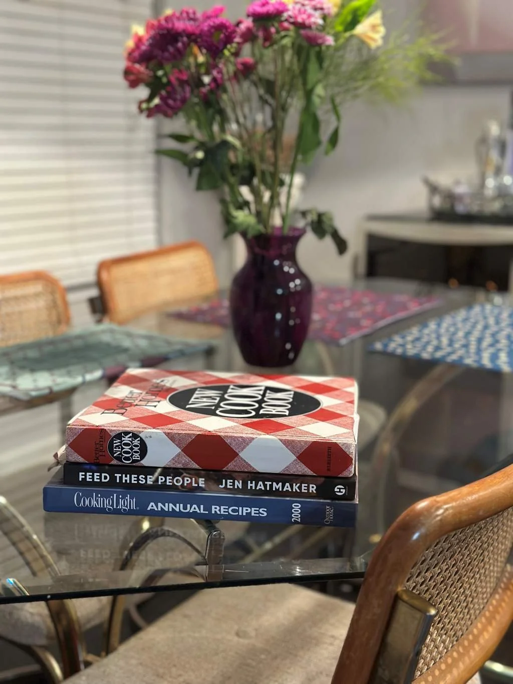 Stack of 3 cookbooks on the corner of a glass table serving as decoration in the dining room.