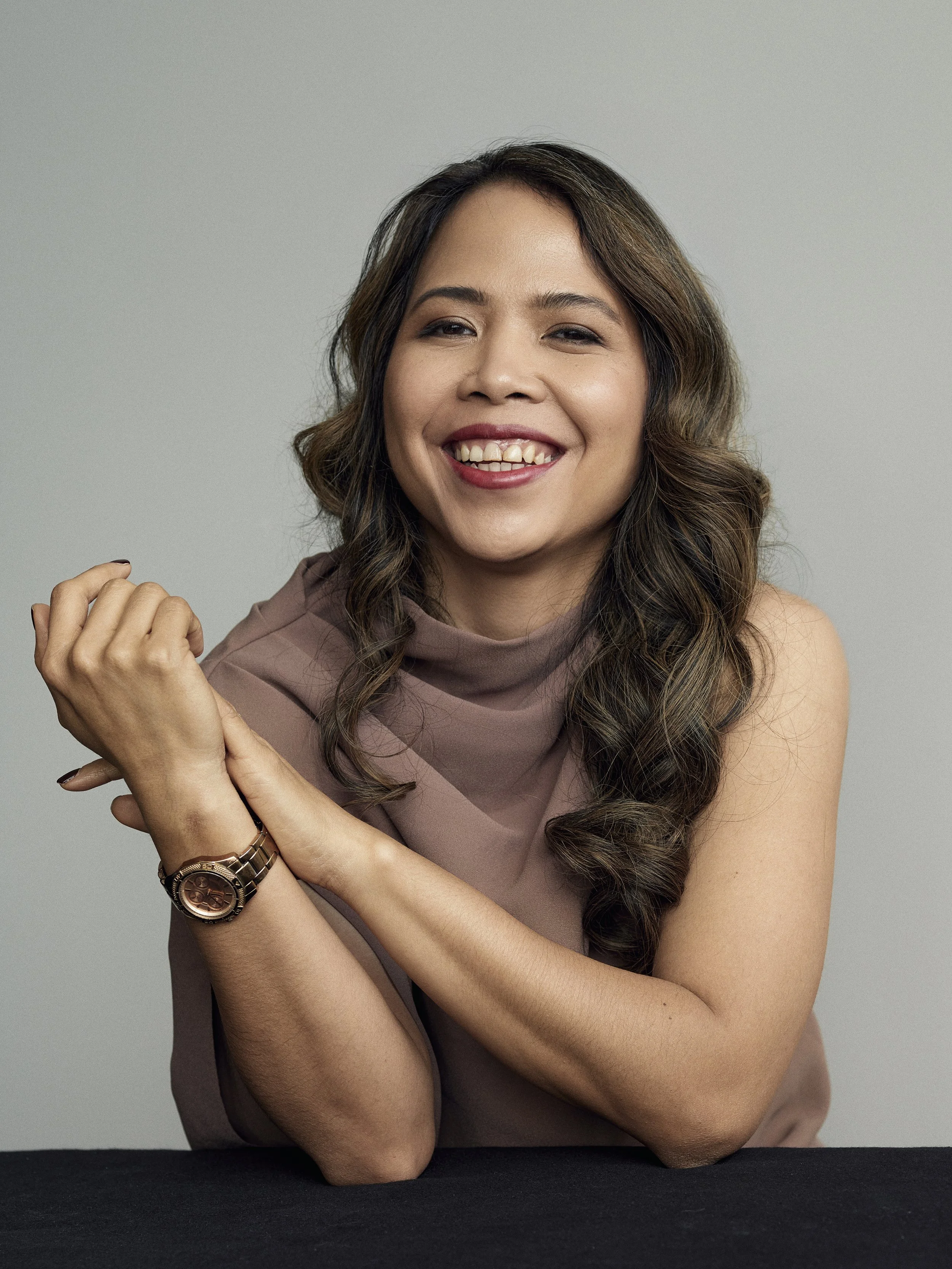 Smiling woman with long brown hair wearing a mauve top and wristwatch