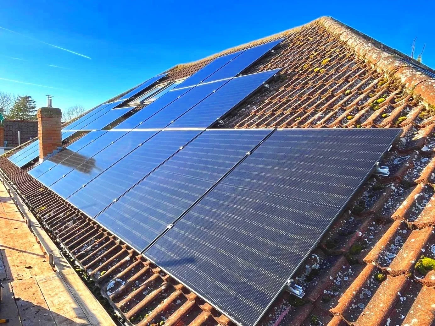 Solar panels installed on a sloped, tiled roof under a clear blue sky.