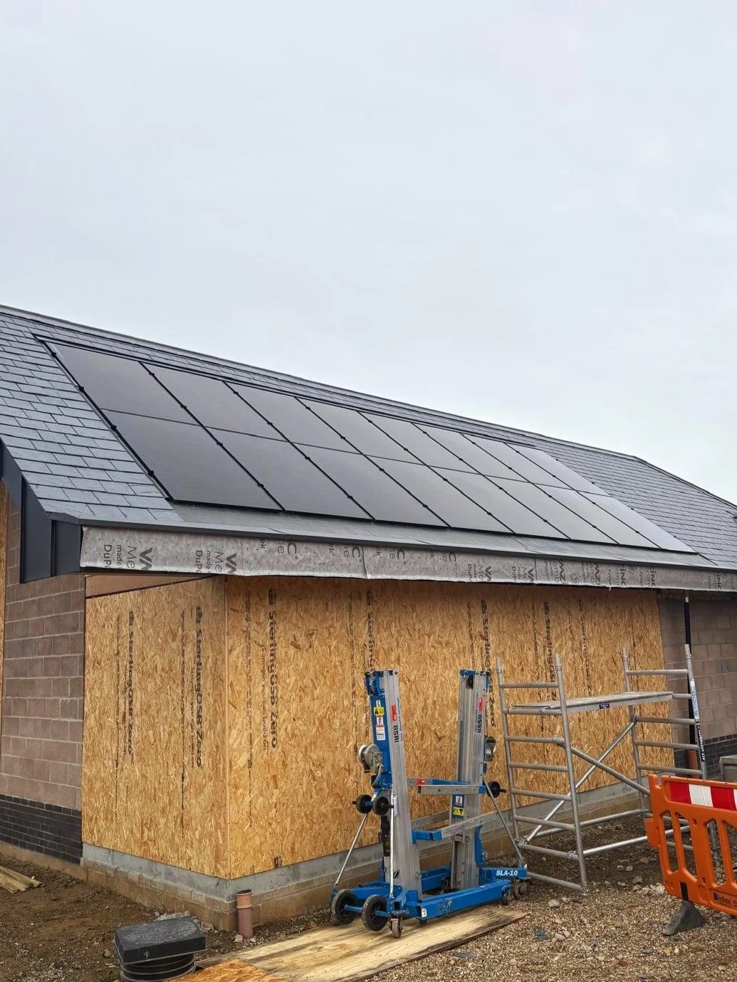 Installation site with a house having solar panels on the roof, and scaffolding and tools nearby.