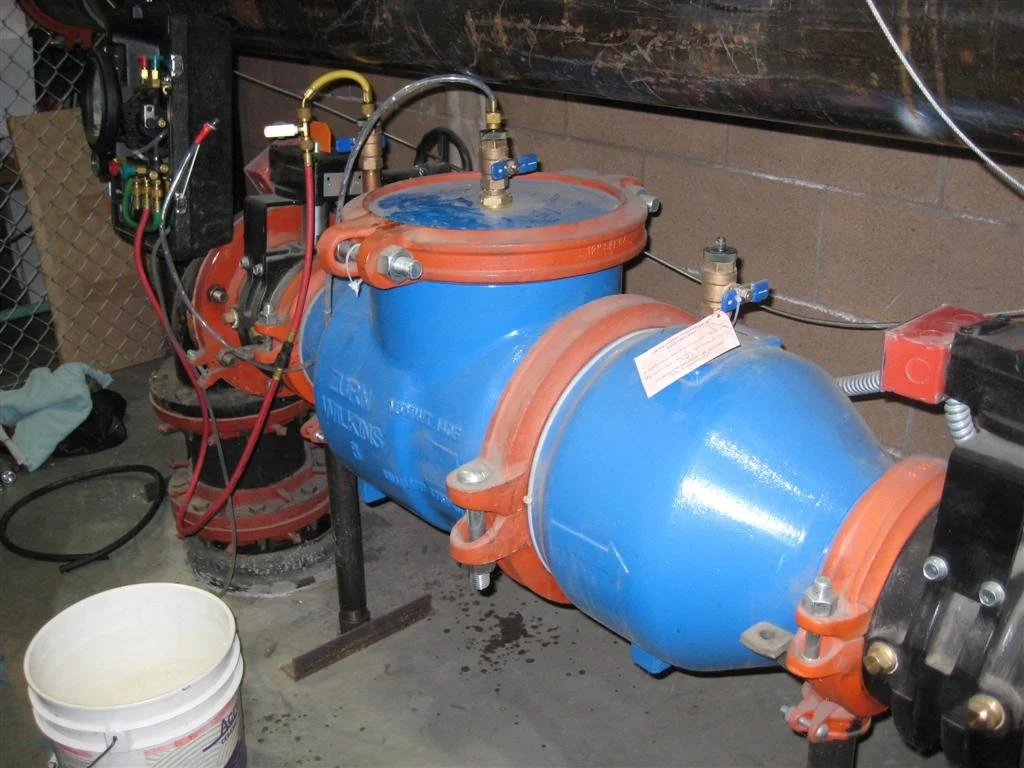 A large blue and orange industrial pump with various pipes and gauges, situated in a workshop or utility room.