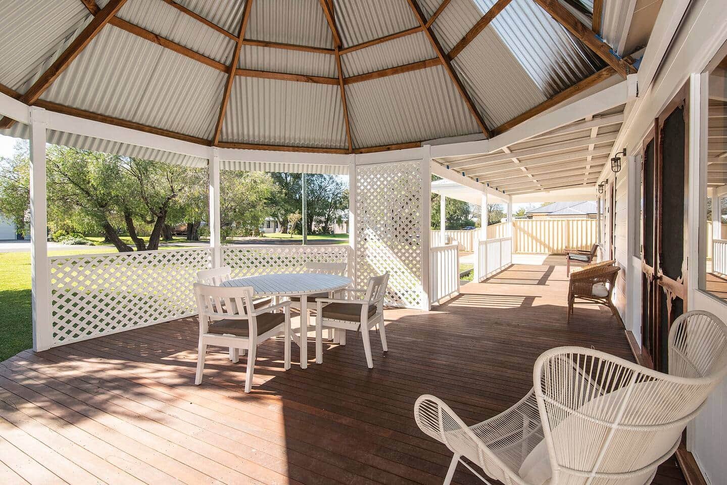Covered porch with wooden flooring, white lattice railing, a round white table with four chairs, and additional seating along the side.