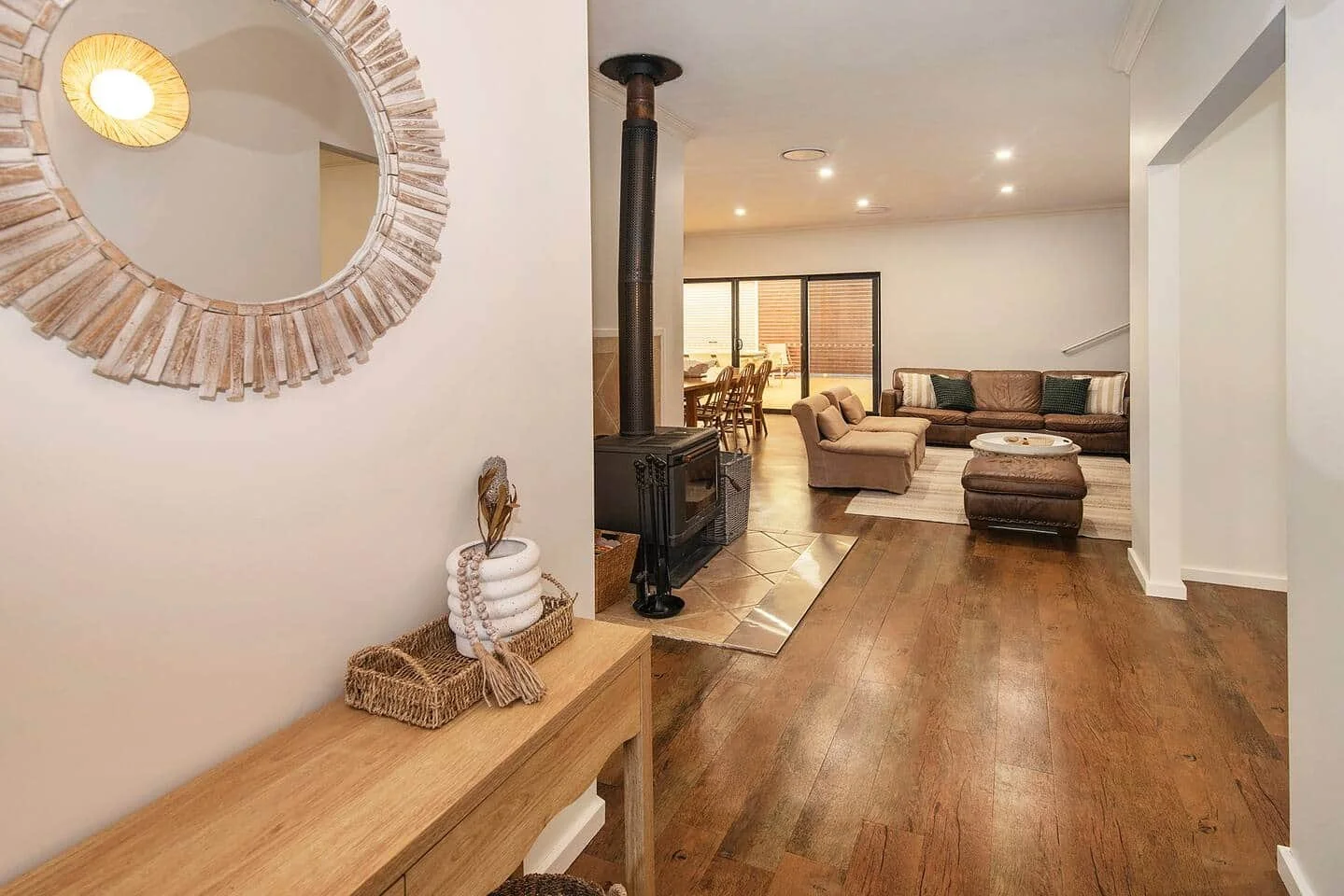 Living room  of holiday house with wood flooring, beige sofas, a dining area, and large sliding glass doors leading outside.