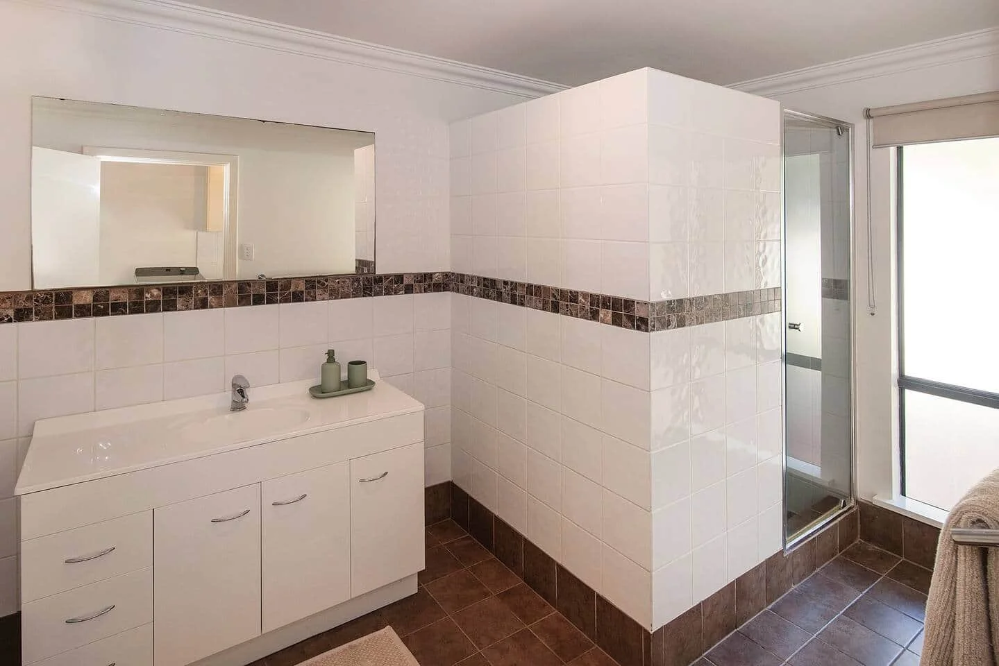 Bathroom with white vanity, large mirror, tiled walls, and a glass shower enclosure next to a frosted window.
