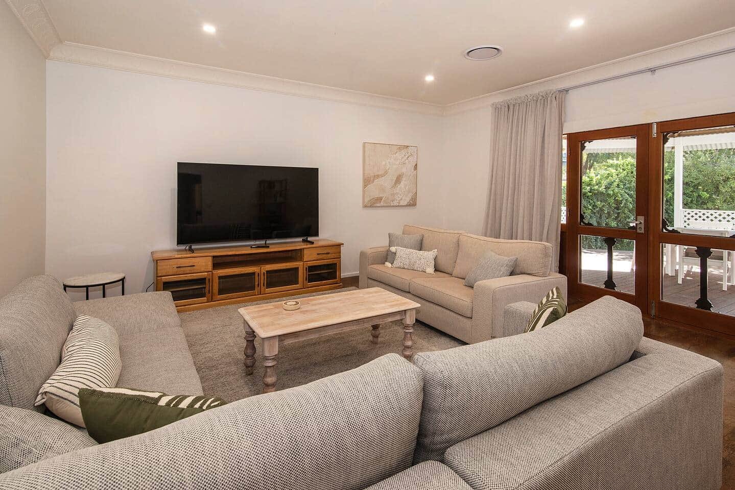 Family living room with beige sofas, wooden TV stand, flat-screen television, coffee table, and large glass doors leading outside.