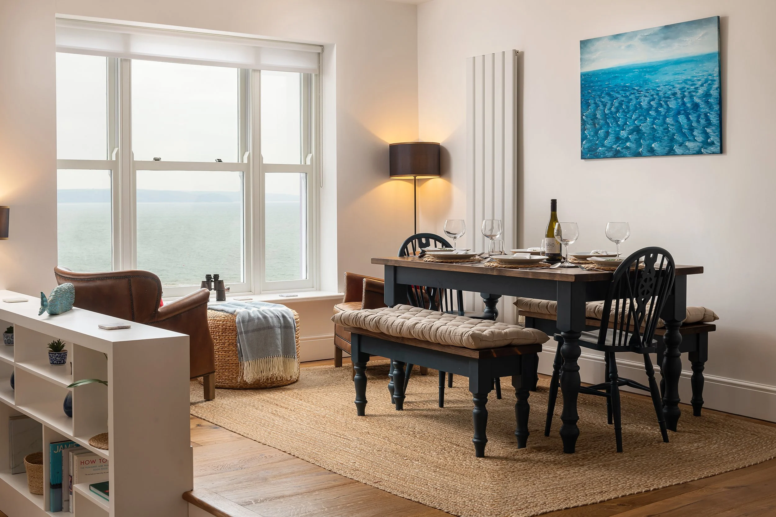 Holiday cottage dining area with a table set for dinner, natural window light and sea views.