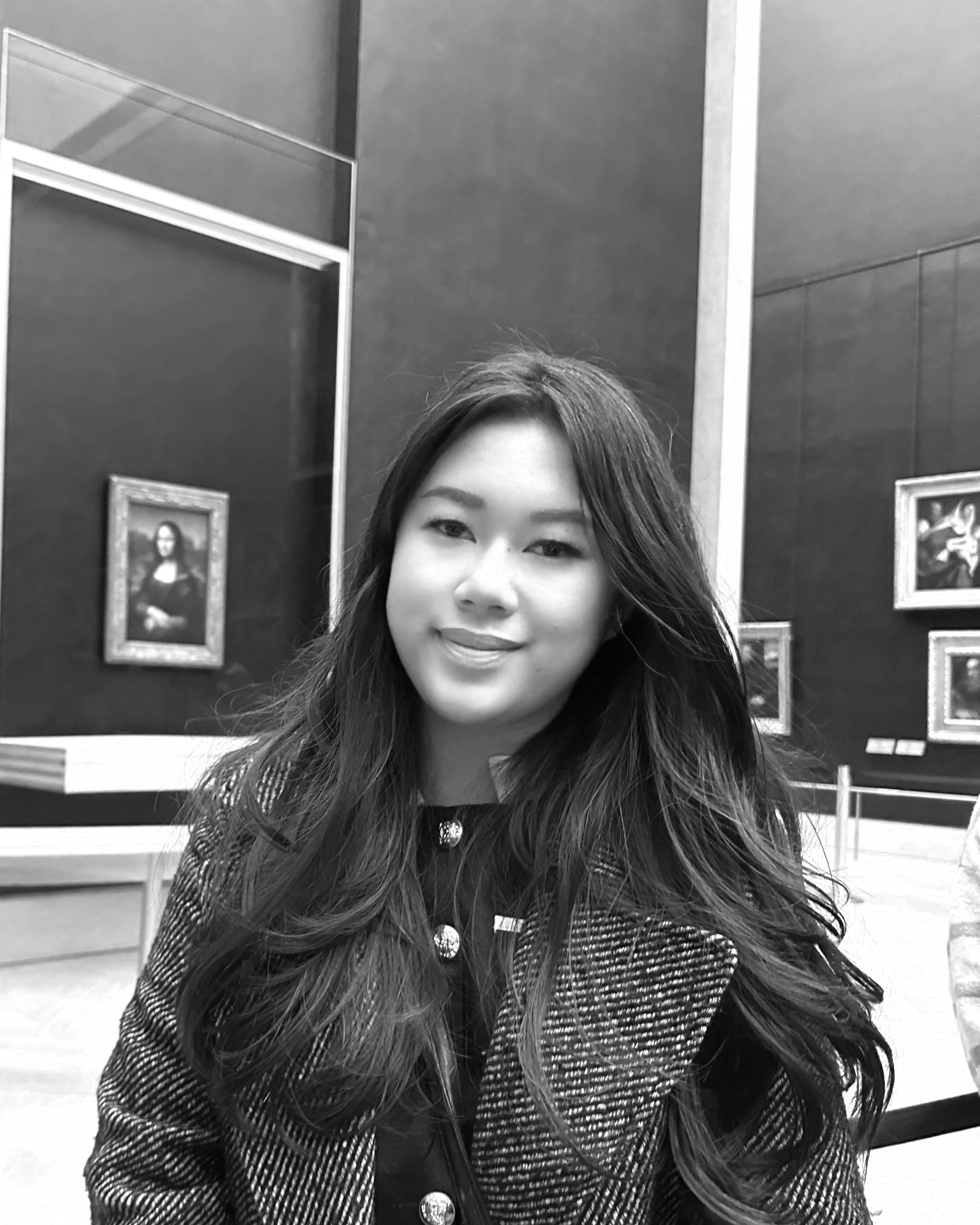 A woman with long dark hair smiling in front of a large sign that reads 'ARRIVAL GALLERY' in black letters, mounted on a wall.