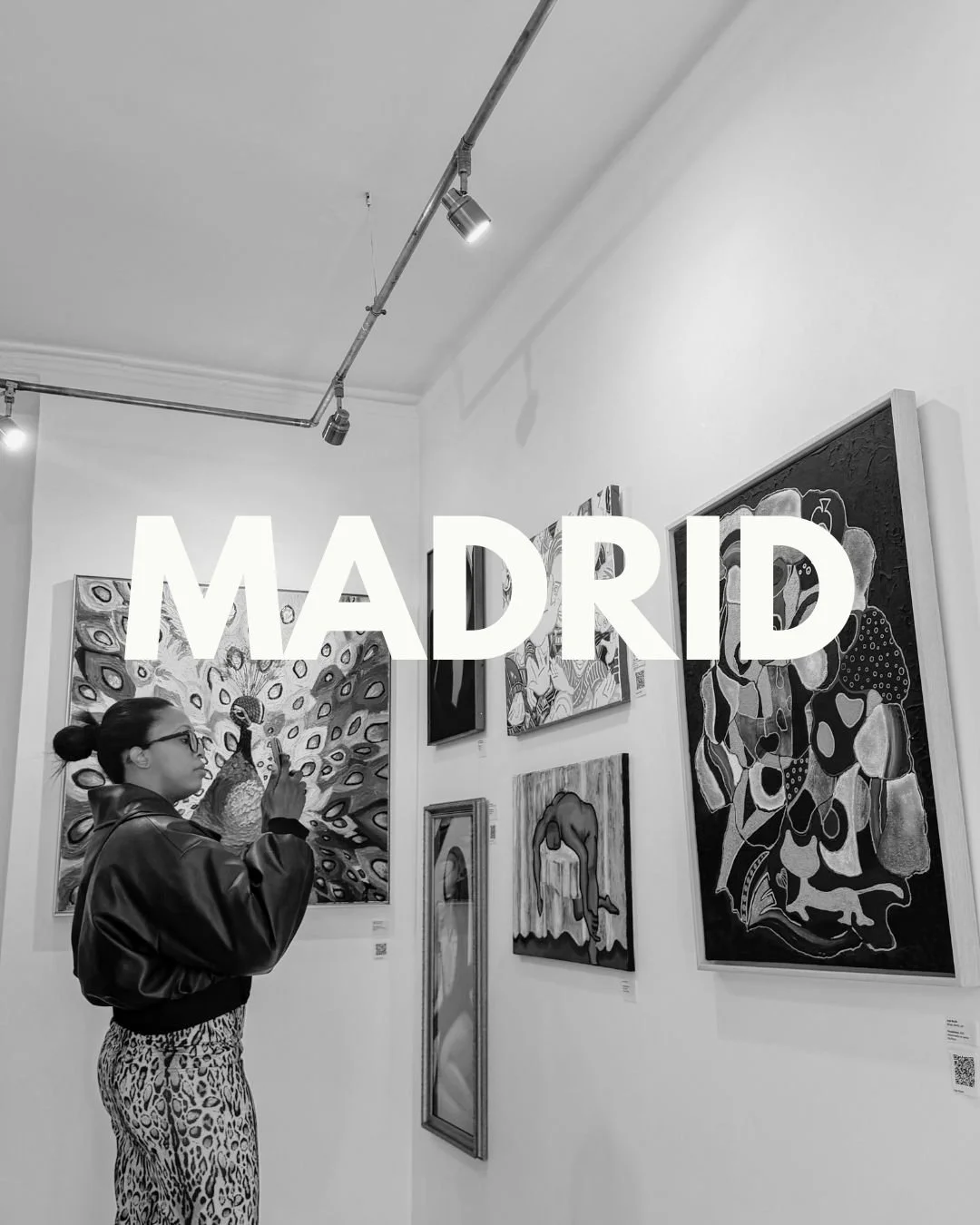 A woman in a leather jacket and animal print pants taking a photo with her phone inside an art gallery with paintings on the wall, and the word 'MADRID' displayed across the image.