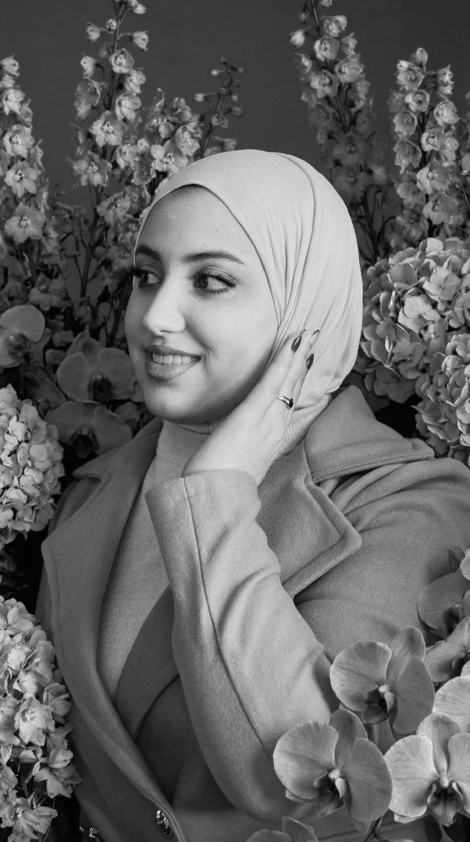 A young man wearing sunglasses, a black T-shirt, shorts, and sneakers standing outside a building with outdoor seating and lantern decorations. He is holding a leash and looking off to the side.