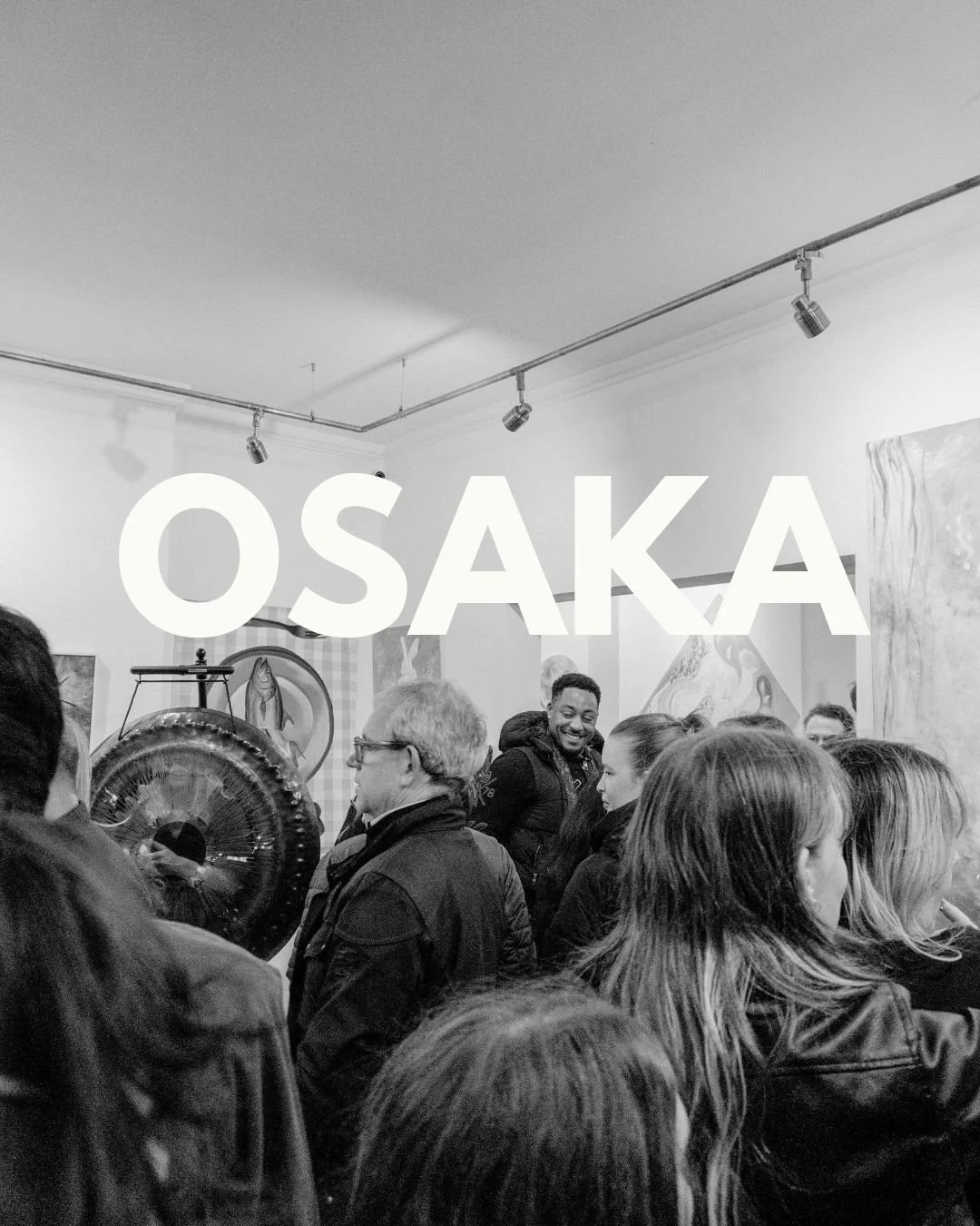Crowd gathered inside an art gallery with paintings on the walls, large white text overlay reading 'OSAKA' in the center.