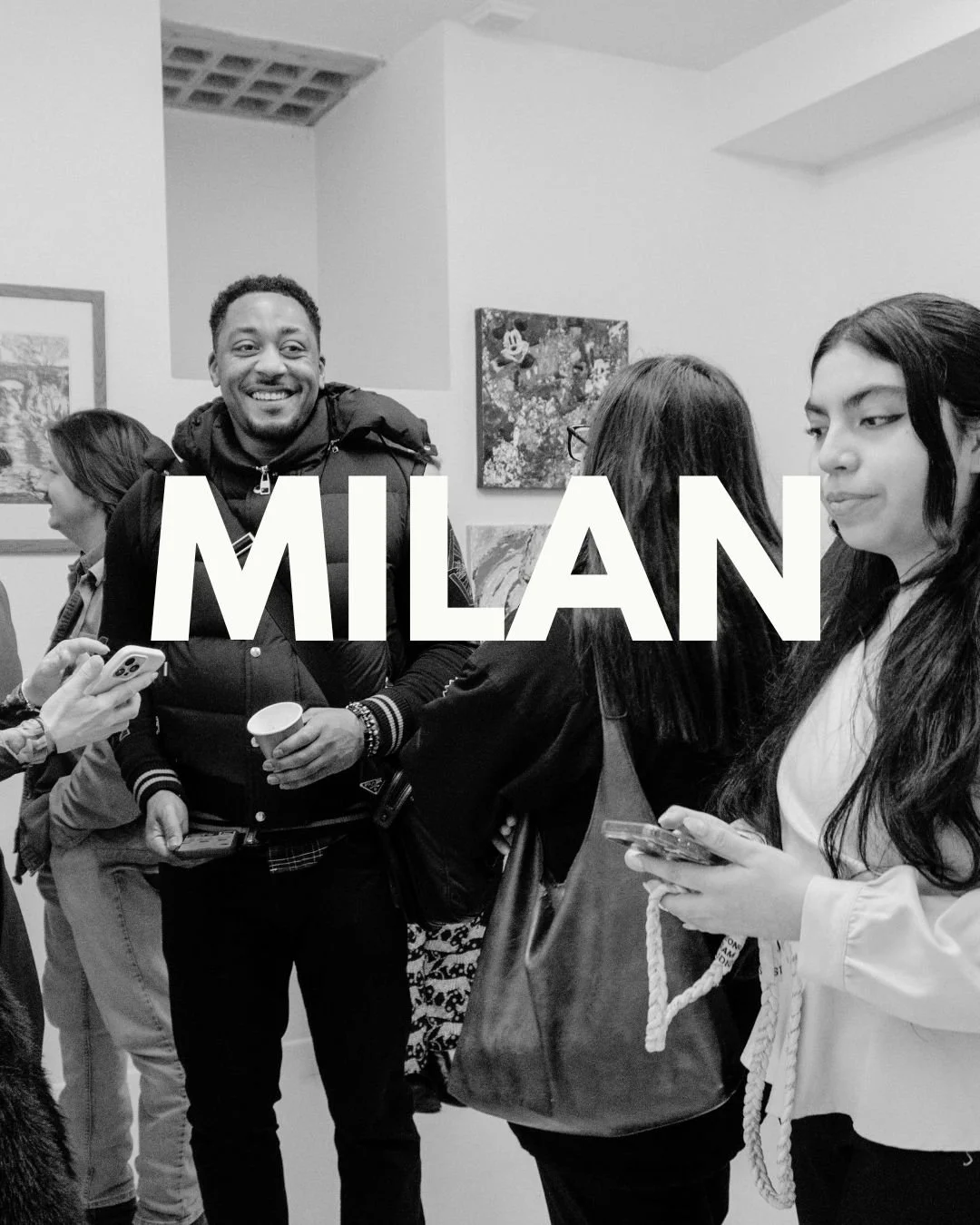 Group of people at an art gallery in Milan, with artwork on the walls and some individuals using smartphones.